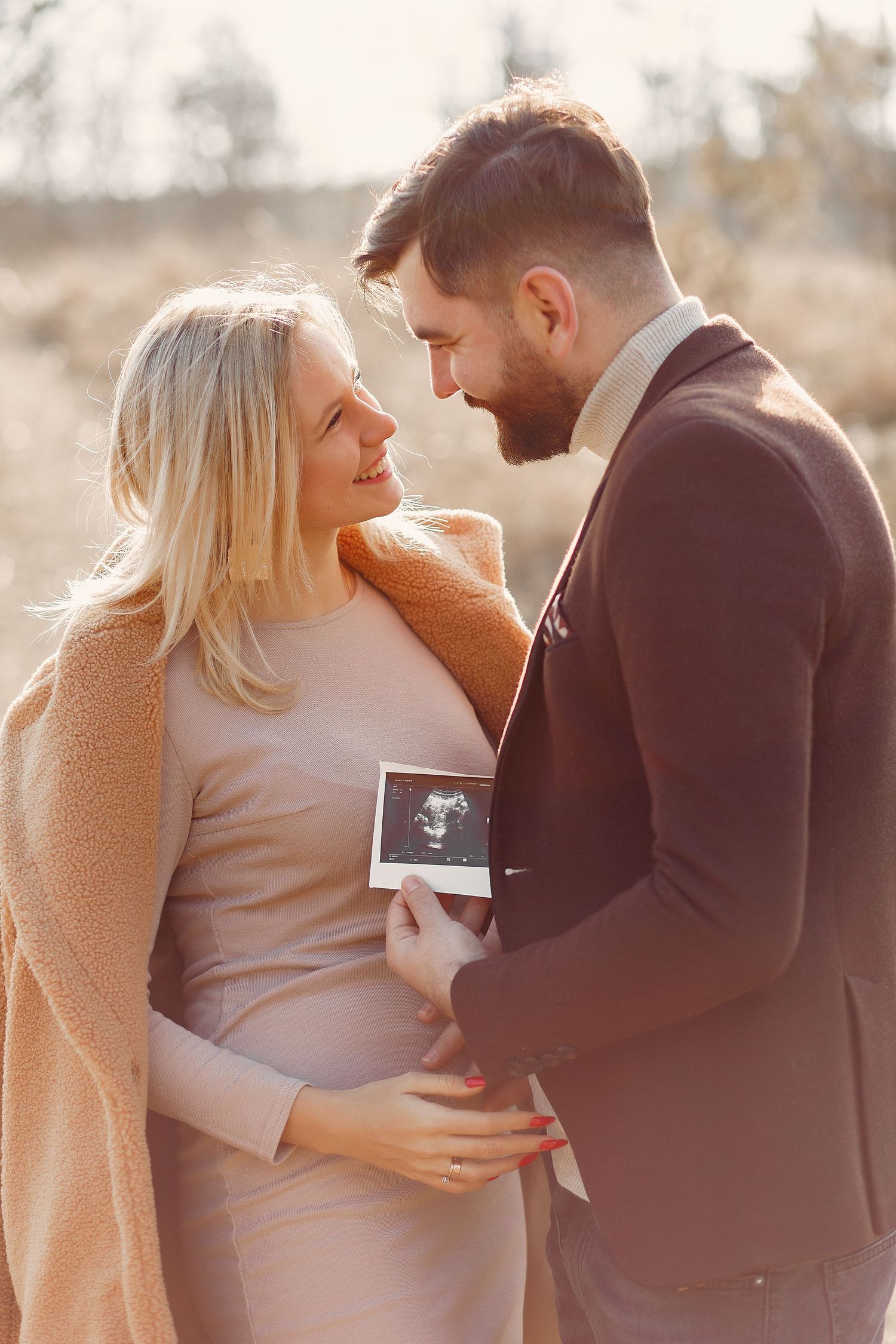 Sunset maternity announcement photoshoot showing couple holding ultrasound photo.