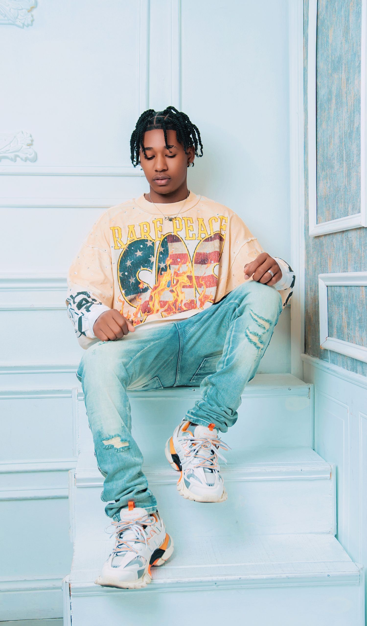 Person wearing peach graphic tee and light jeans sitting on white bench.