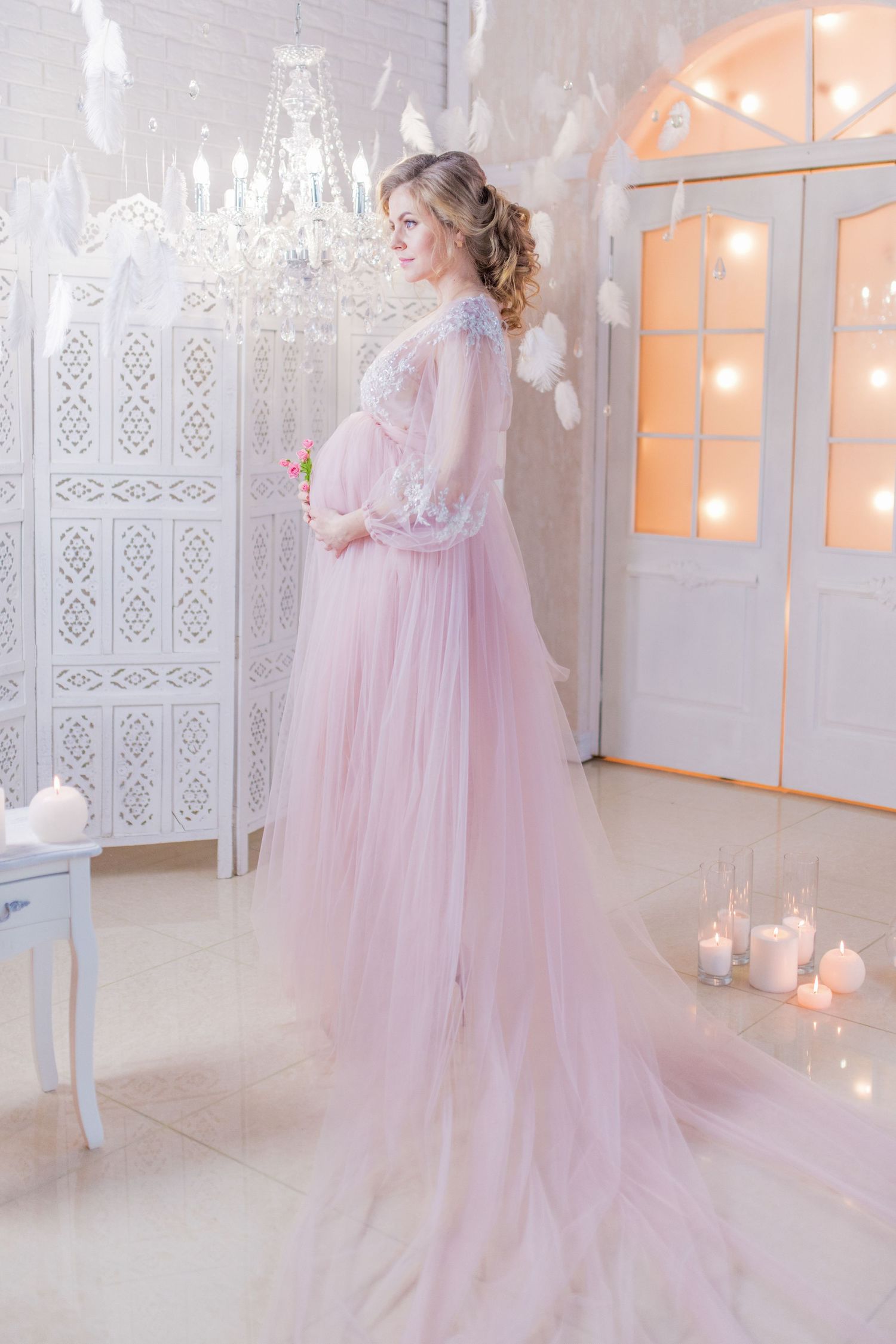 Dreamy maternity session with flowing pink tulle gown in white room with candles.