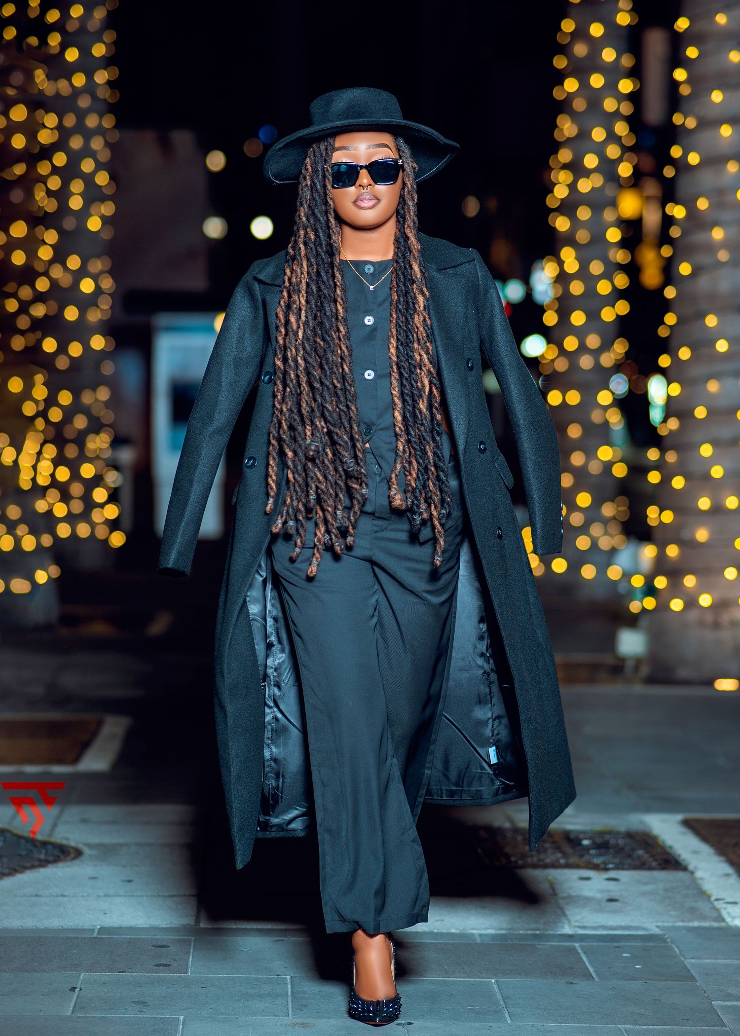 Stylish portrait with long braids and black blazer against glowing bokeh lights.