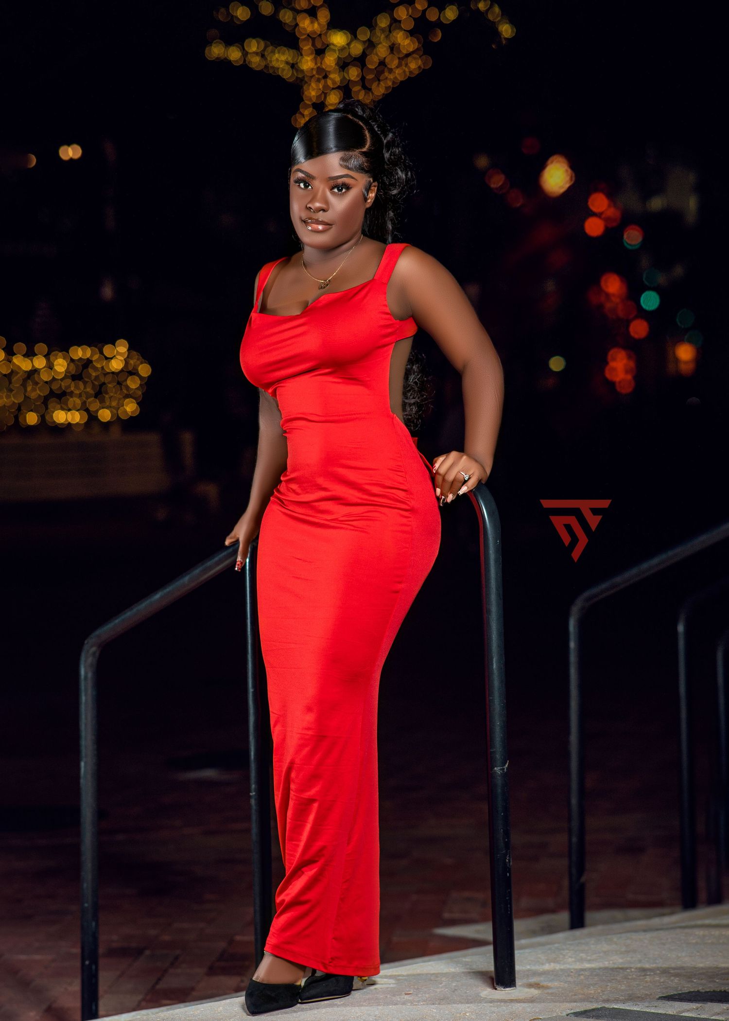 Striking red floor-length dress worn elegantly against nighttime city lights.