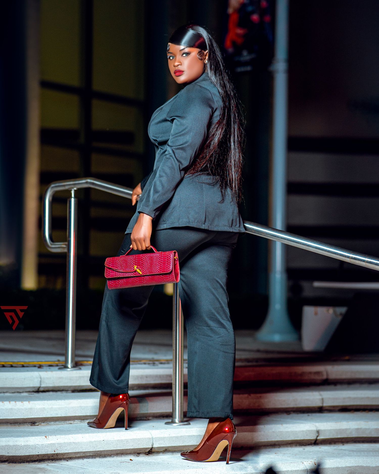 Business chic outfit with gray suit and red handbag on urban steps.