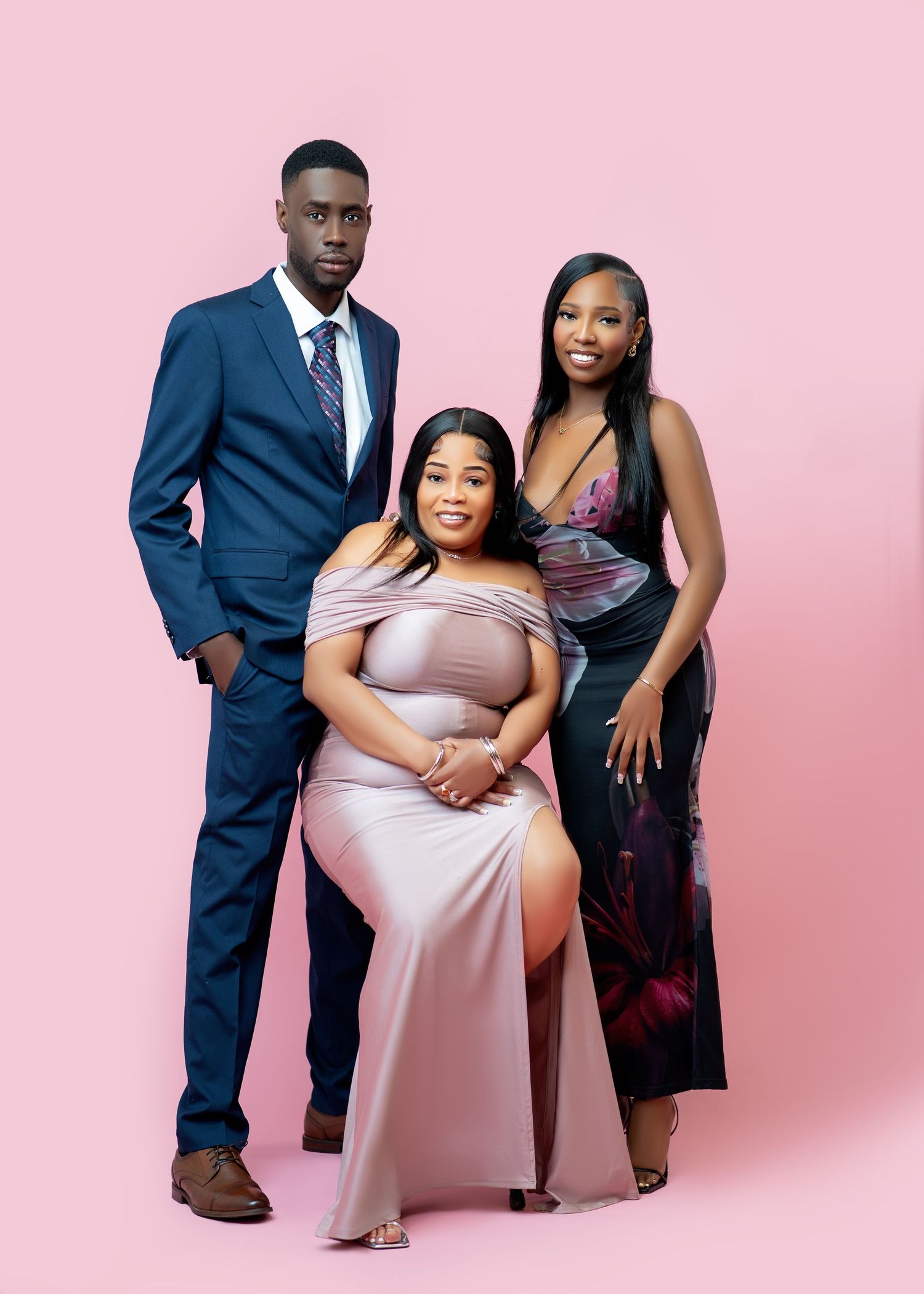 Three elegantly dressed young adults pose together against a pink background in formal attire for a professional portrait.