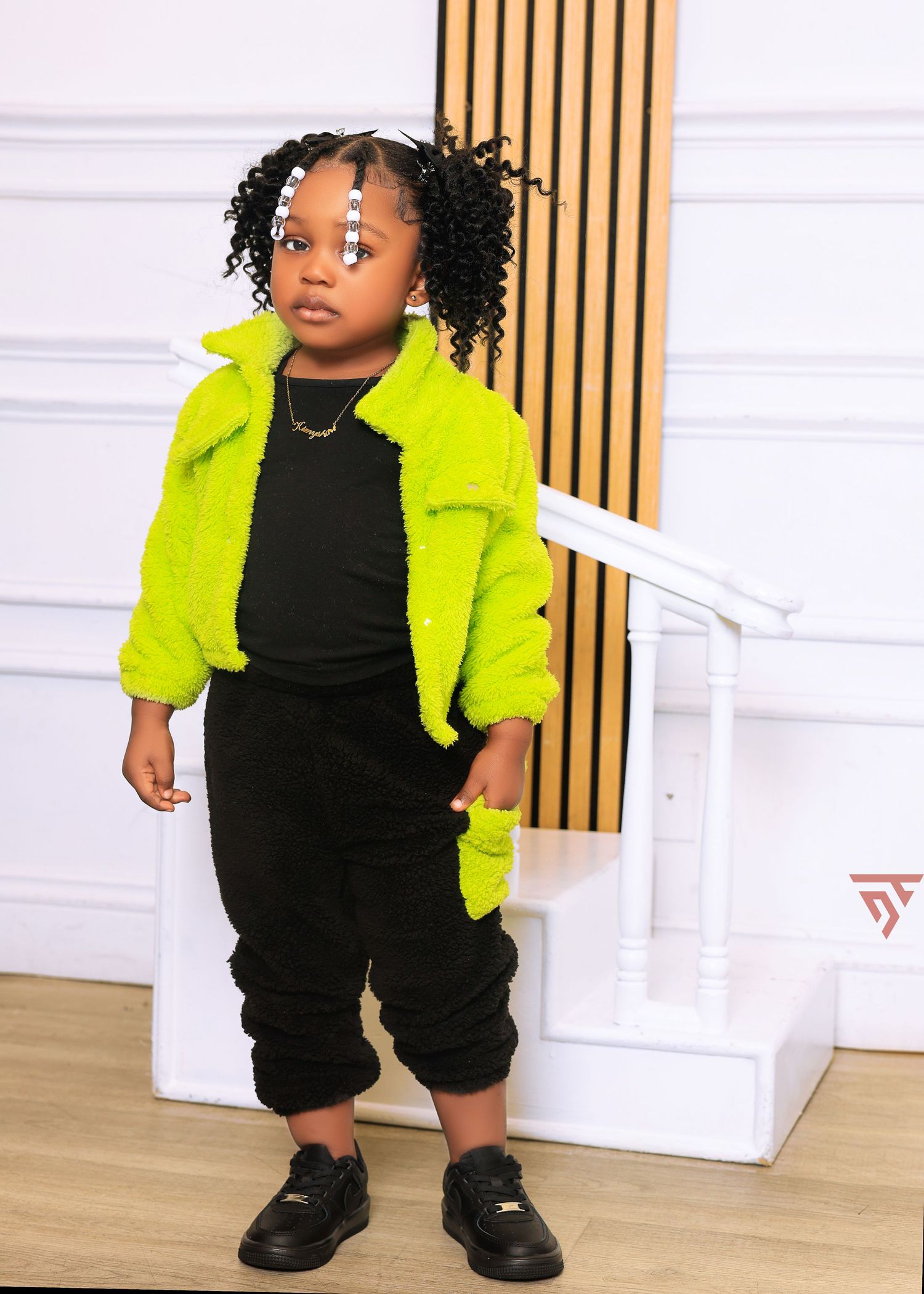 Young child wearing bright neon yellow jacket and black pants poses against white wall with wooden accents.