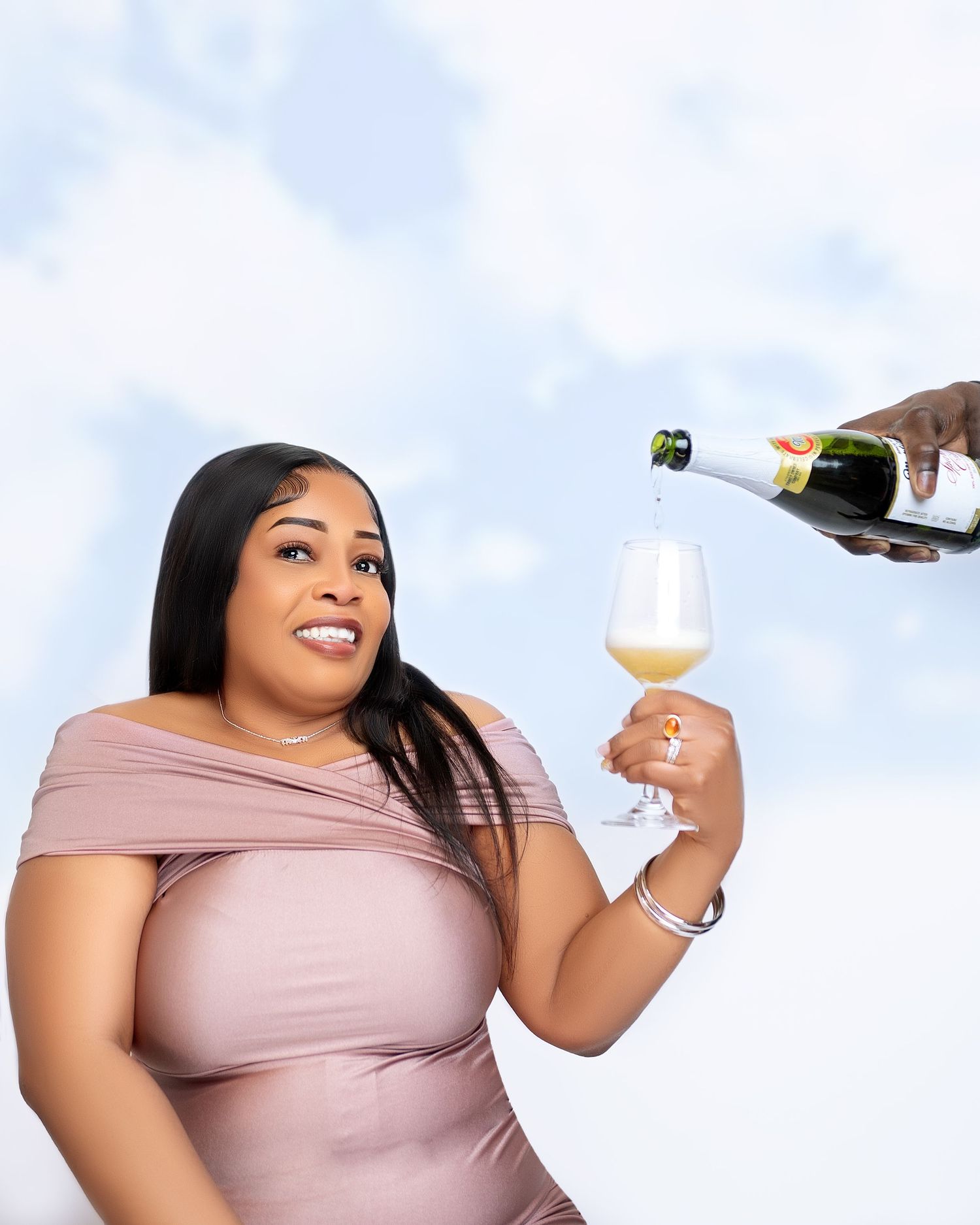 Woman in pink off-shoulder dress holding wine glass being poured white wine against cloudy sky backdrop.
