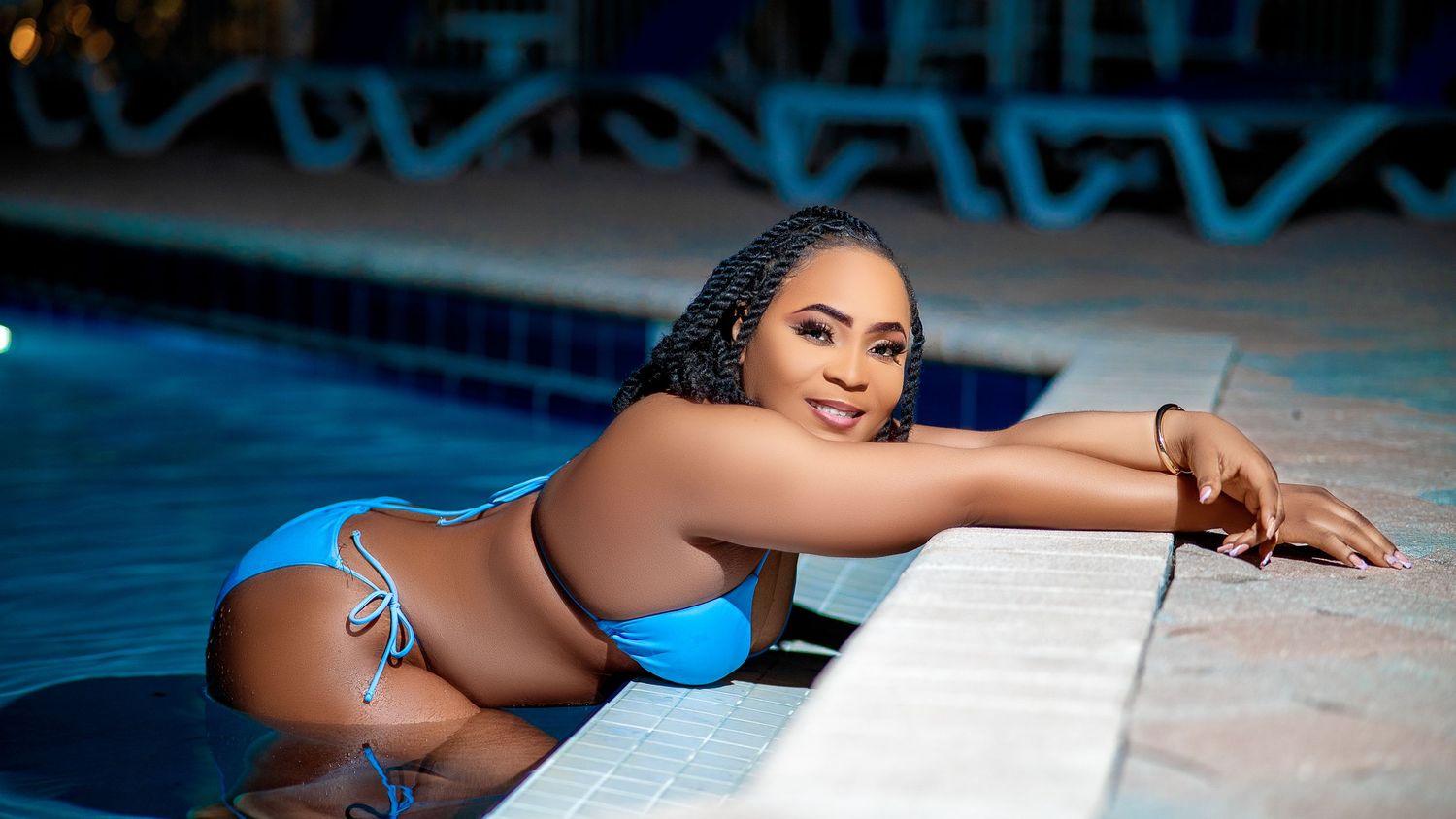 A person in a blue swimsuit relaxes on a pool ledge during a sunny day.