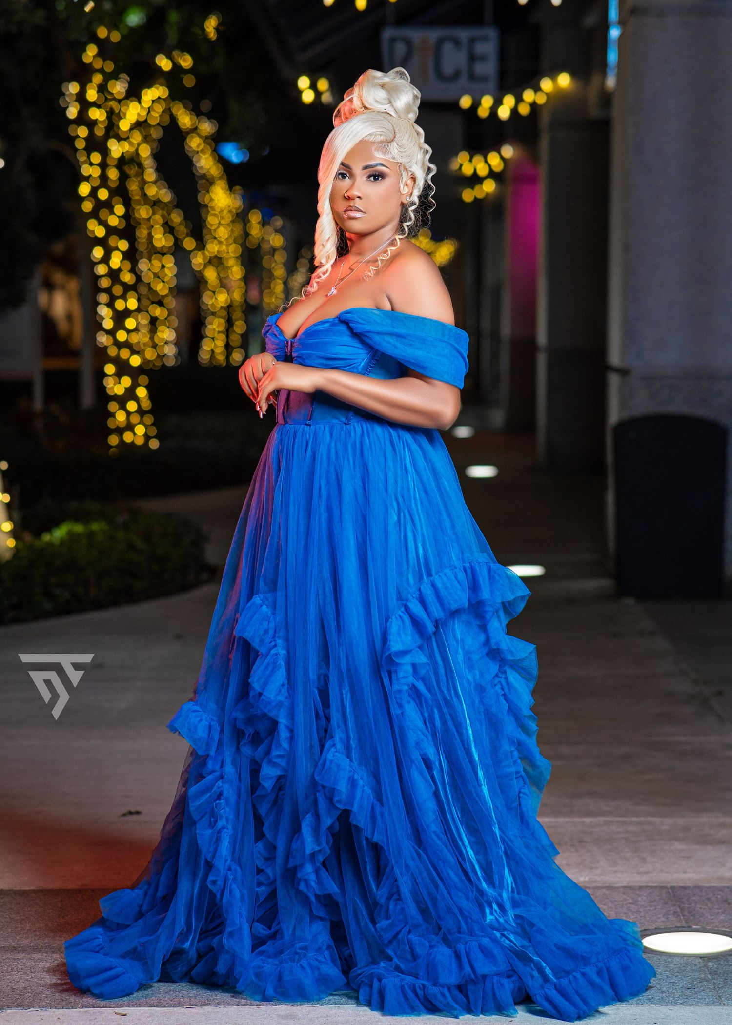 Dramatic flowing blue off-shoulder gown photographed against twinkling lights.