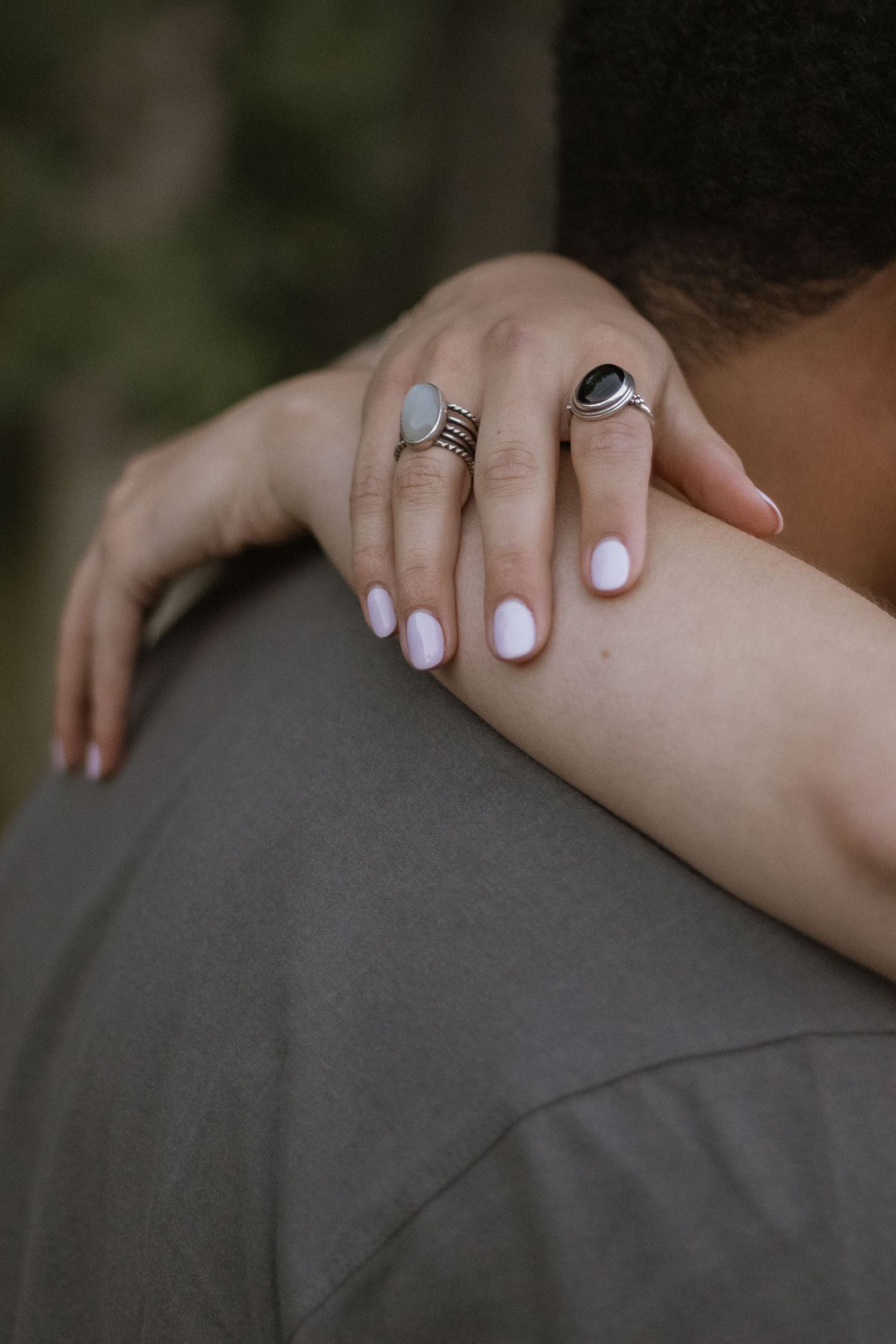 Close-up of hands with white nail polish gently resting on a grey shirt.