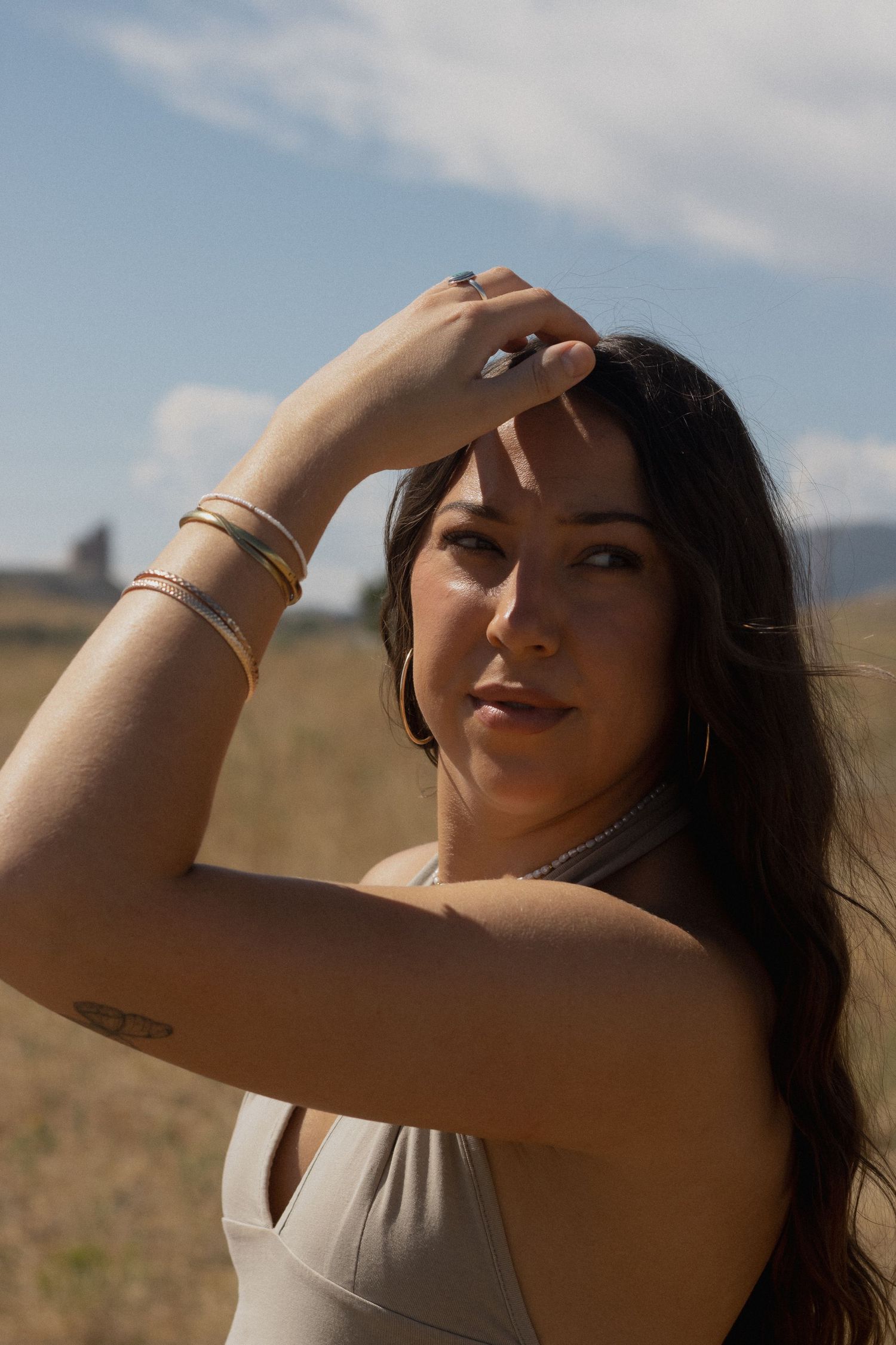 Person with jewelry shielding eyes from bright sunlight in mountain field.