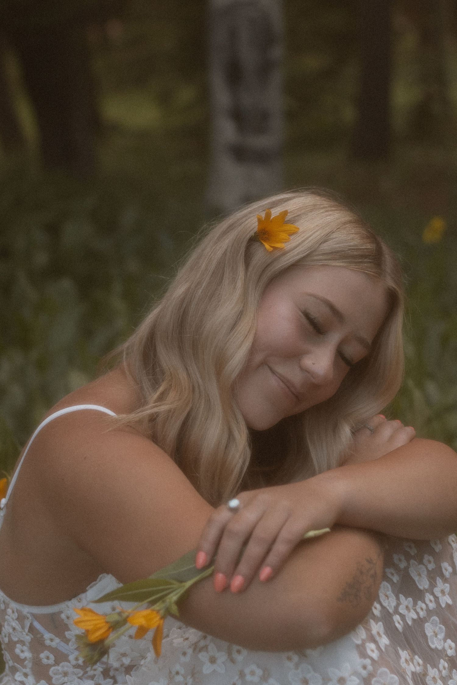 Woman in white lace dress rests peacefully among wildflowers in a dreamy outdoor setting.