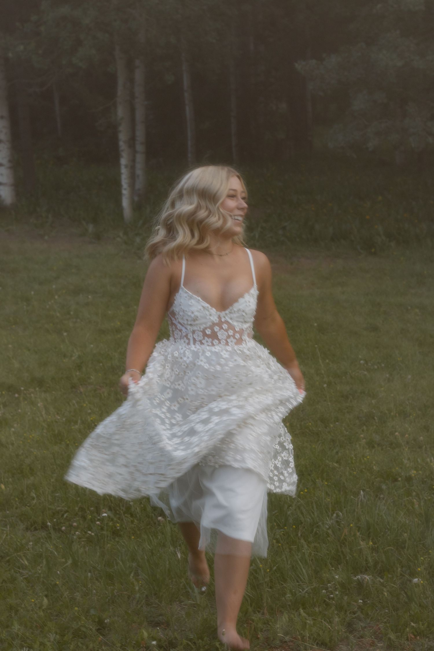 Person twirling in a white lace dress outdoors in a grassy field at dusk.