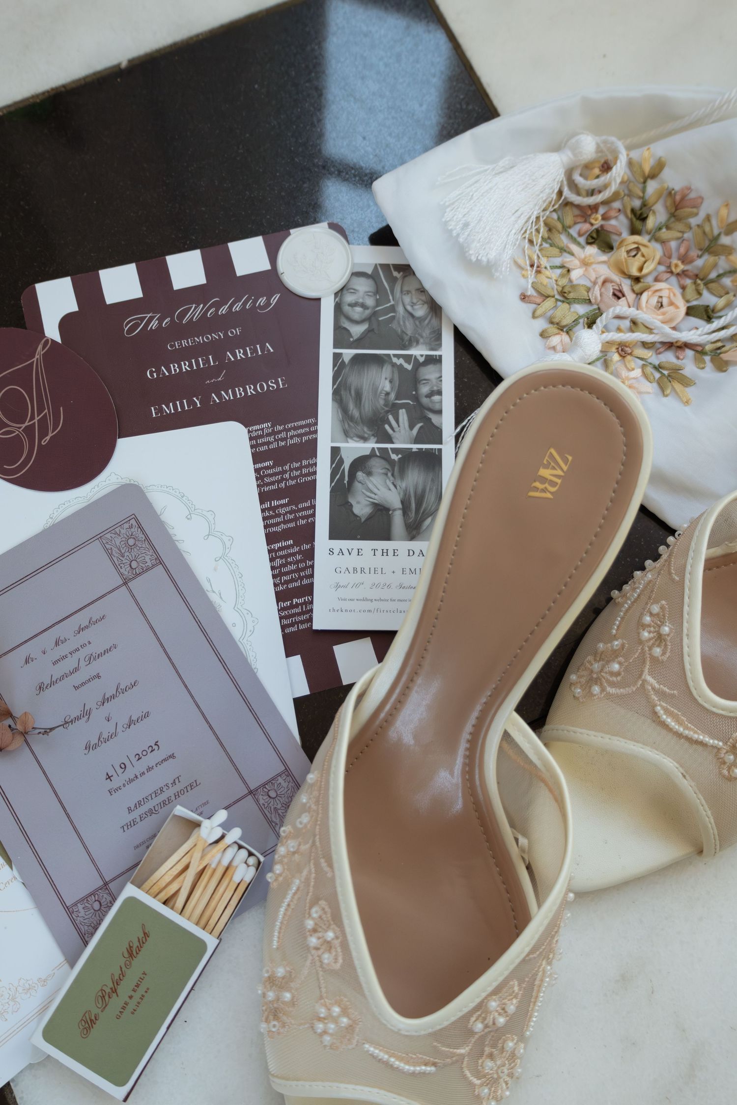 Elegant wedding flat lay featuring cream heels, floral bouquet, save the date cards, photo booth strips, and matchbooks on marble.
