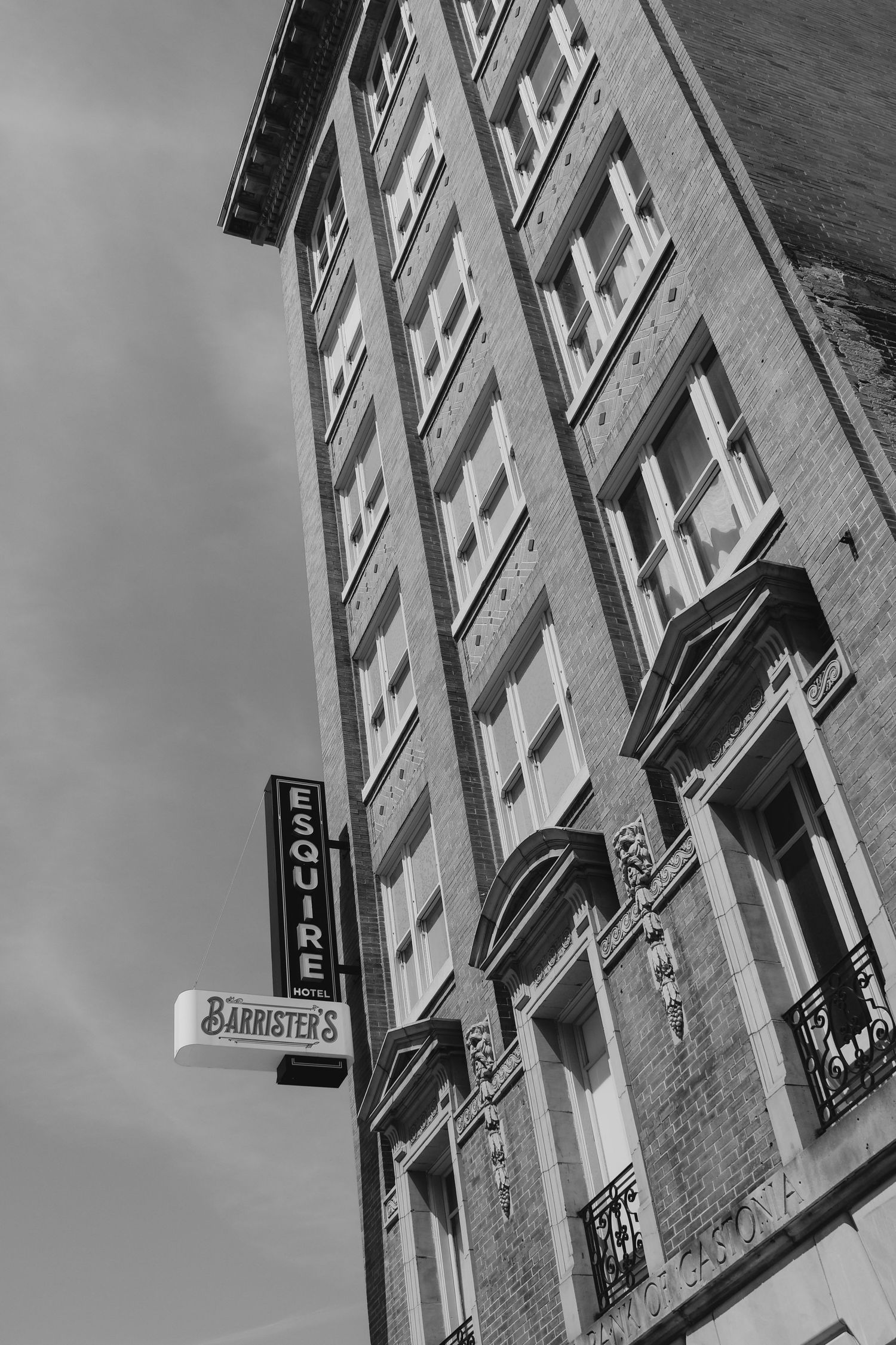 Black and white photo of a tall brick building with Esquire and Barristers signs, shot from below.