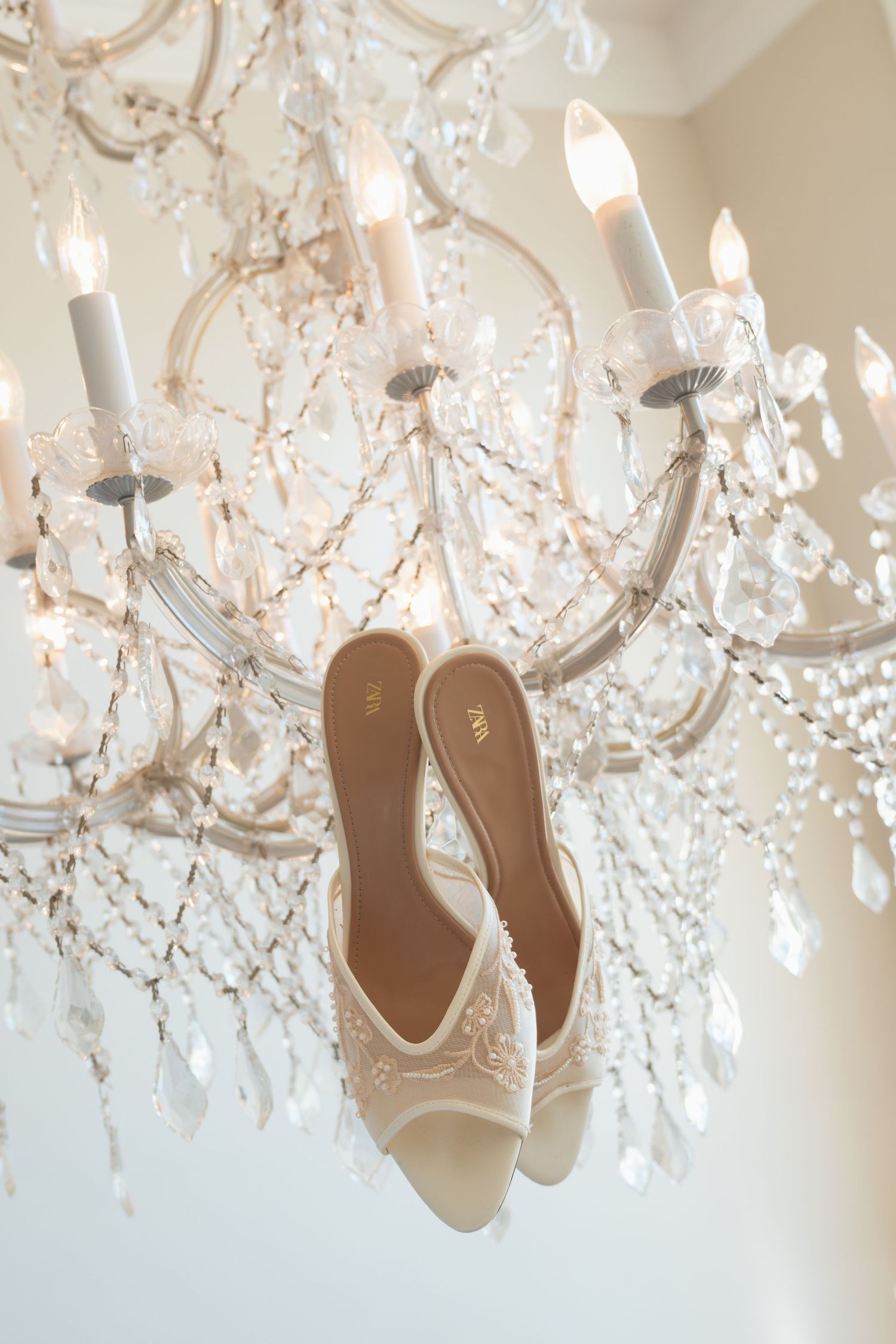 Elegant white bridal heels hanging from a crystal chandelier, perfect for a luxurious wedding day detail shot.