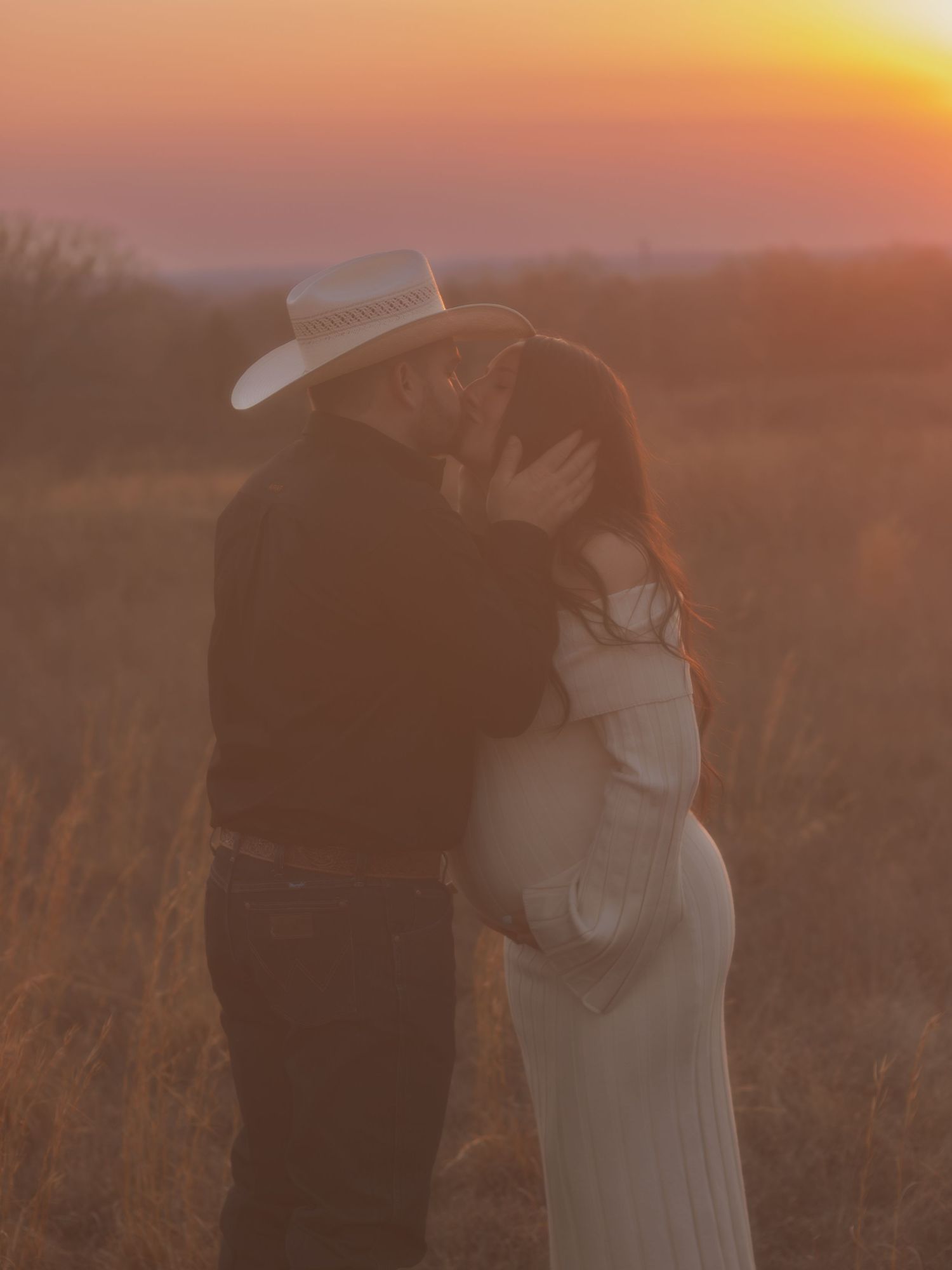 A couple embraces in a golden wheat field at sunset creating a romantic silhouette against the warm sky.