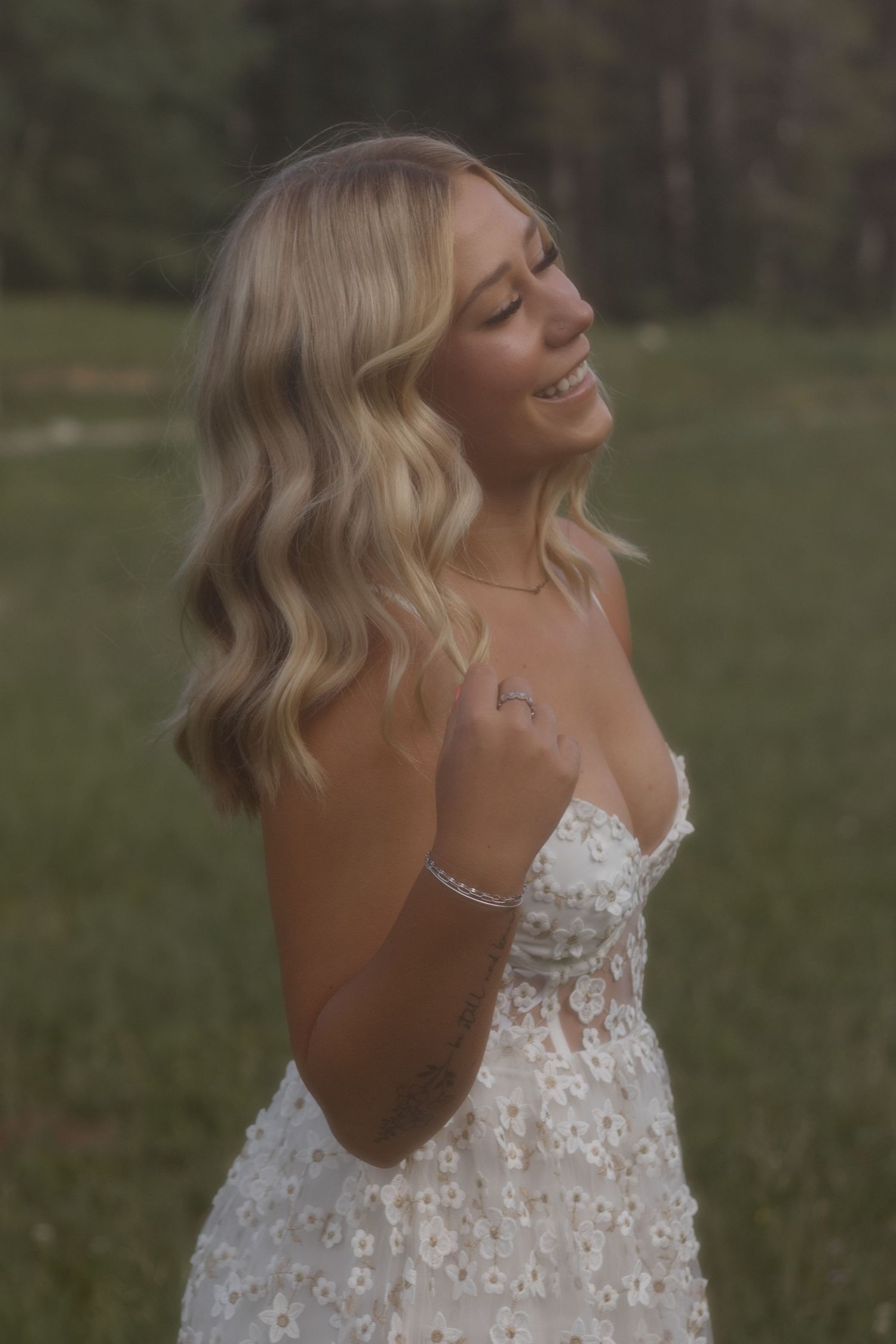 Woman in white lace dress twirls joyfully in an outdoor nature setting.
