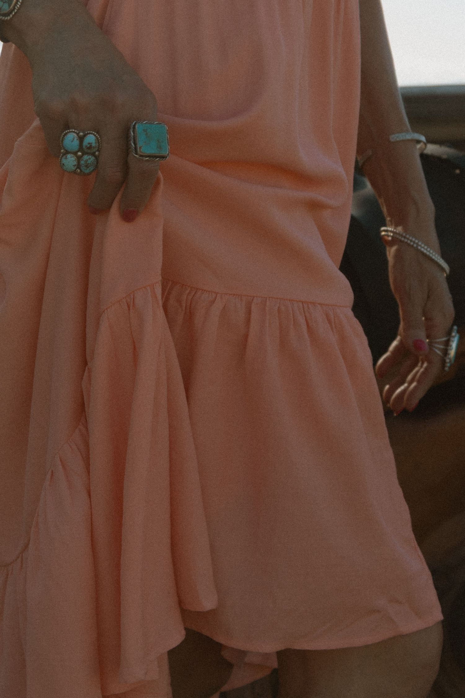 Woman in peach tiered mini dress wearing turquoise rings and bracelets, boho western jewelry styling.