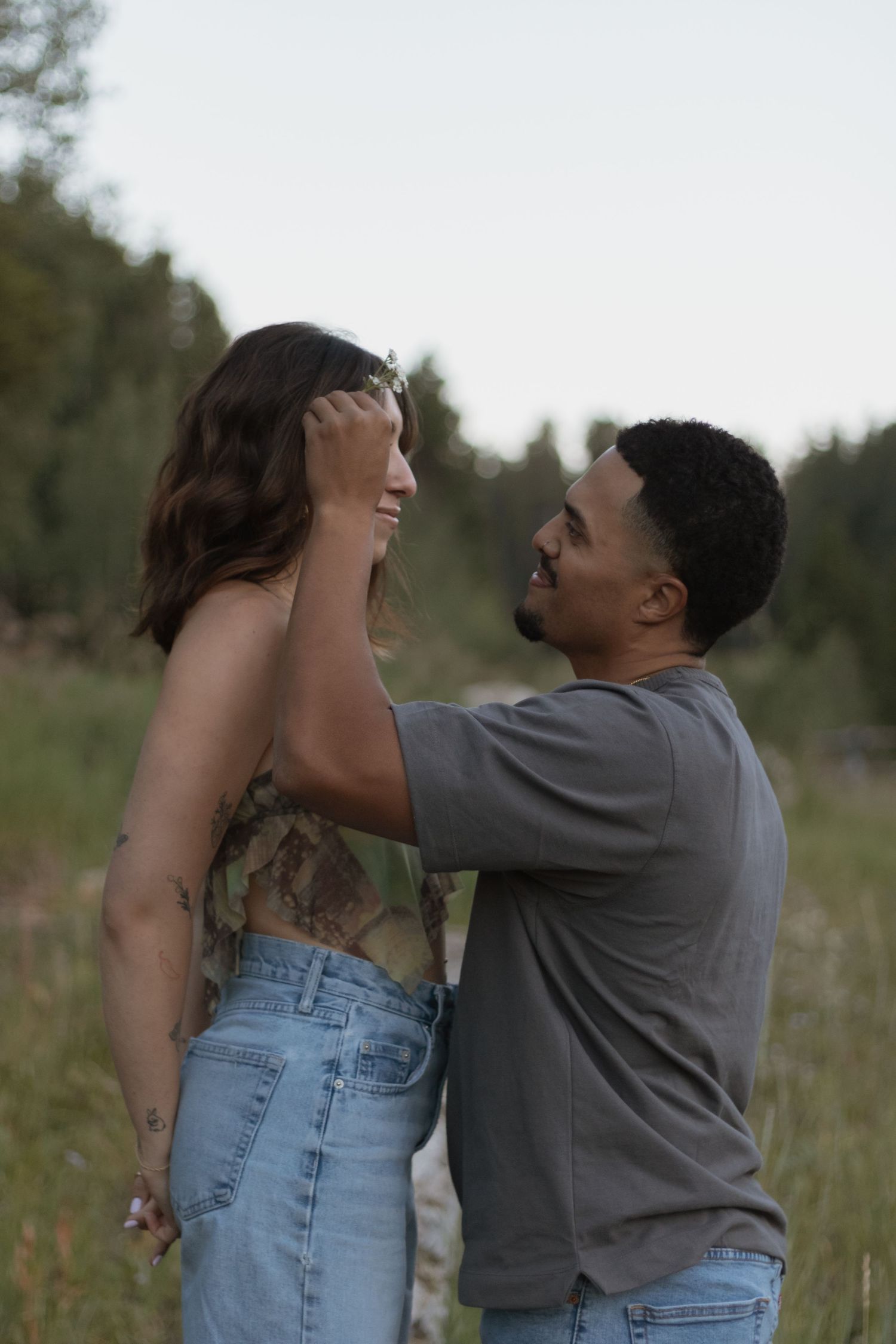 Couple embracing in a field with tall grass and trees in the background.
