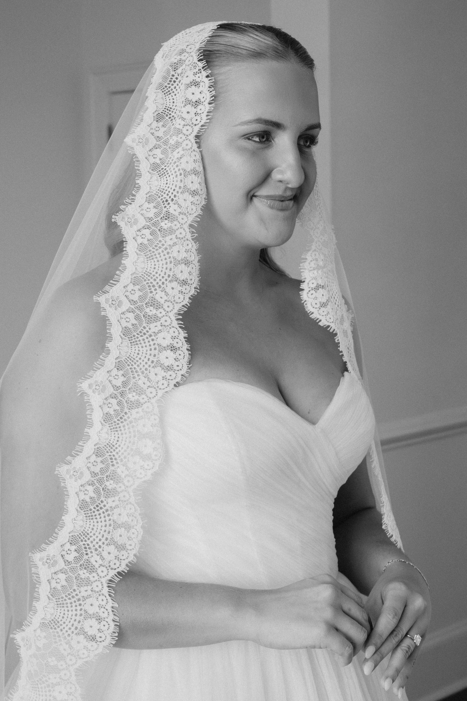 Black and white portrait of a smiling bride wearing a lace-trimmed veil and strapless wedding gown.