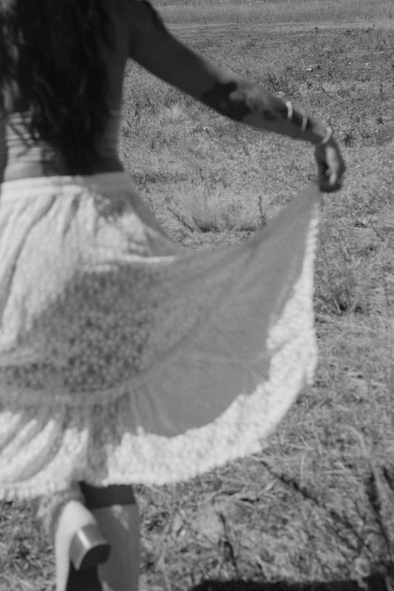 Black and white image of someone twirling in a flowing white lace skirt in a field.