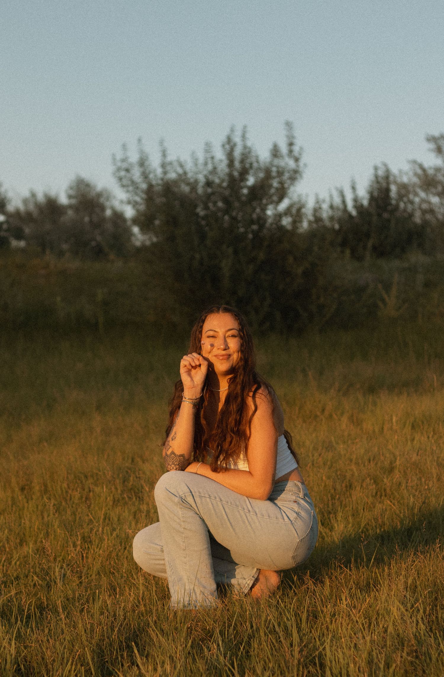 Person in casual wear sitting relaxed in sunlit grass field during golden hour.