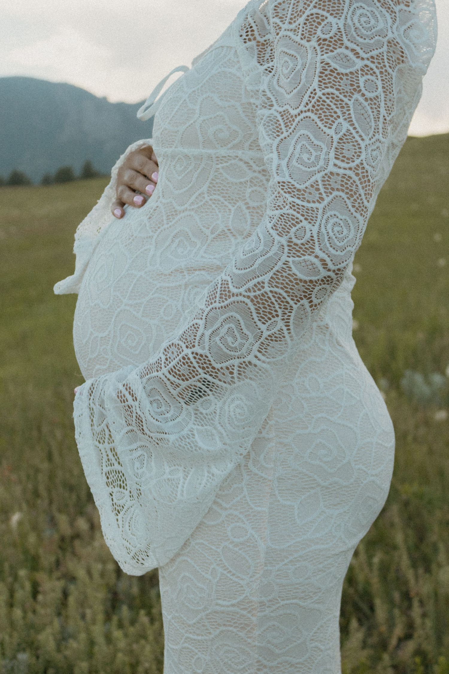 Close-up of delicate white lace details on a flowing dress against a mountain backdrop.