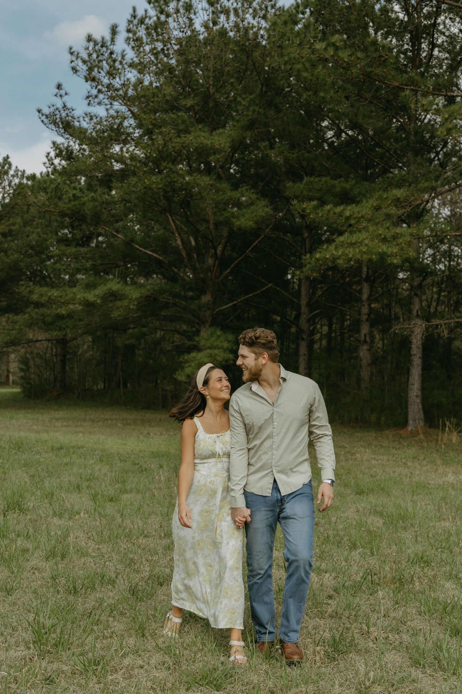 A couple shares an intimate moment while walking through a green field.