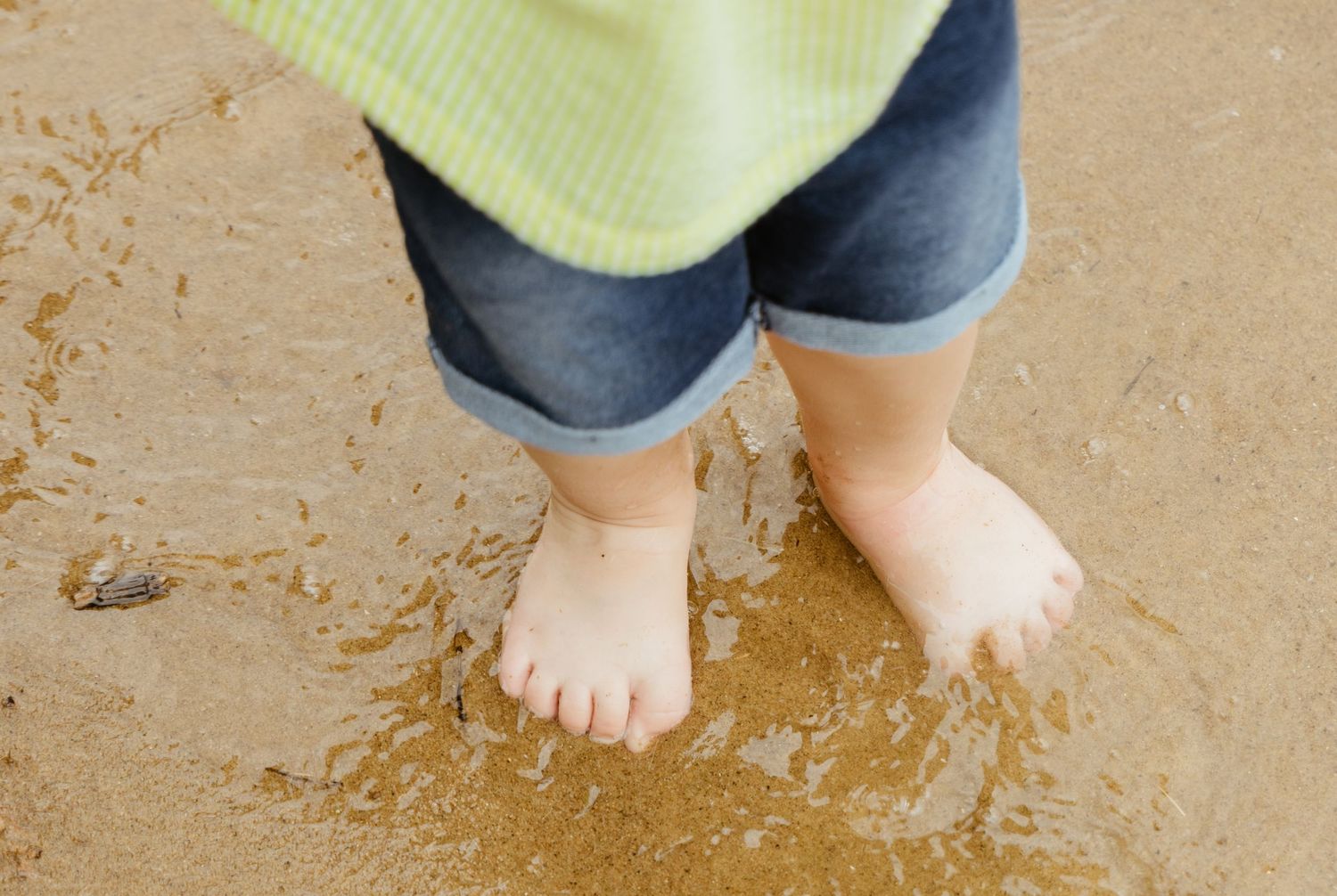 Small bare feet standing in shallow sandy water.
