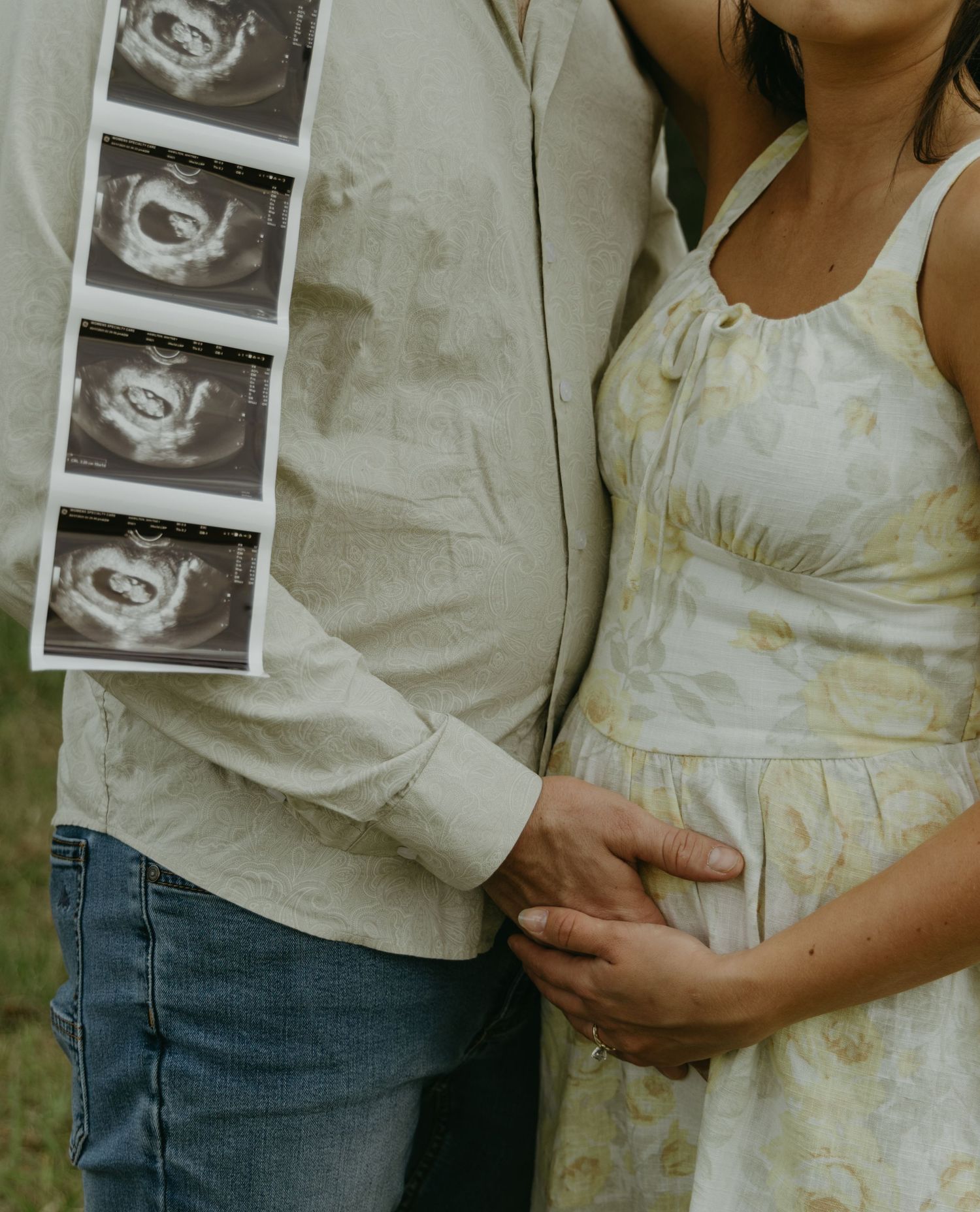 Tender moments captured as a couple displays their ultrasound photos in a field.