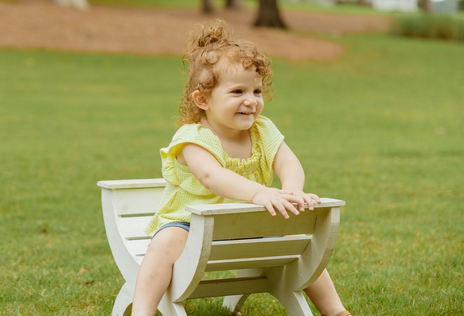 Children sitting and playing on white chairs on a grassy lawn.