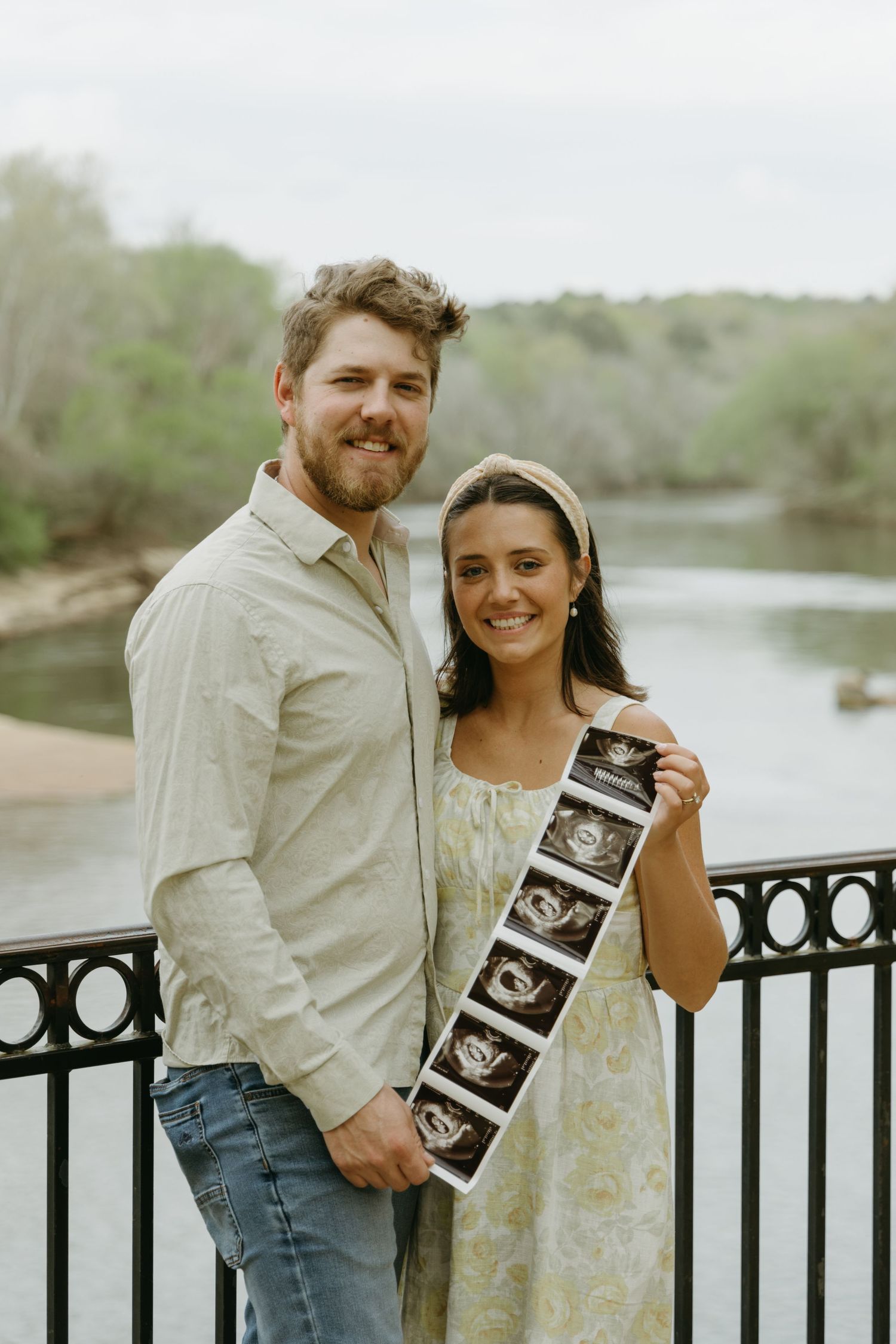 Happy couple holding ultrasound photos by a waterfront railing.