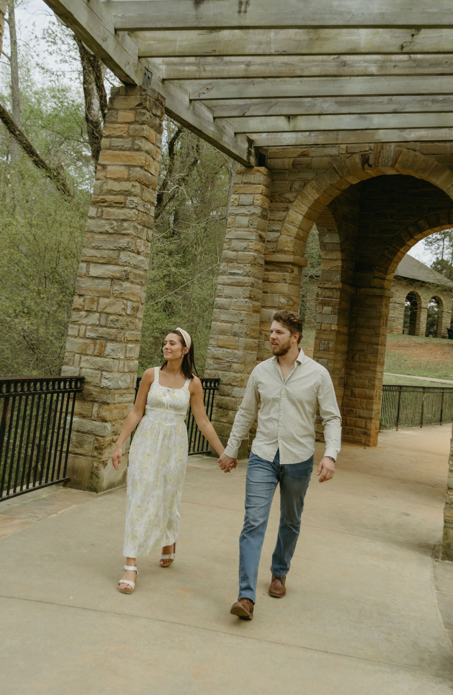 Couple walking hand in hand through a covered stone walkway.