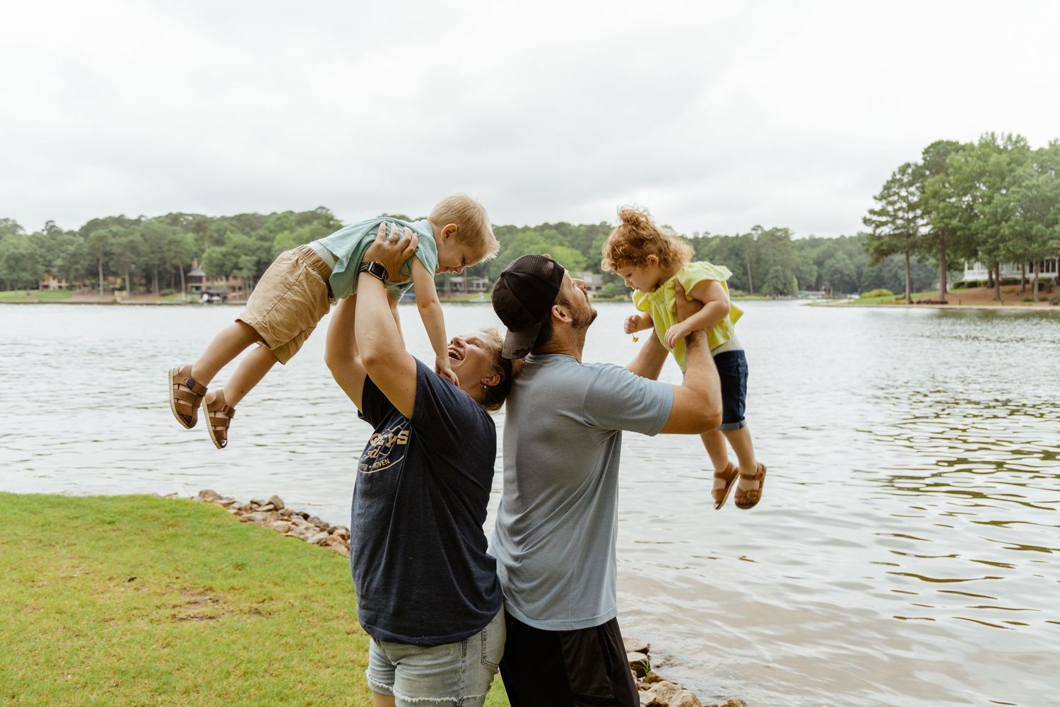 Family members playing and lifting children near a lake.