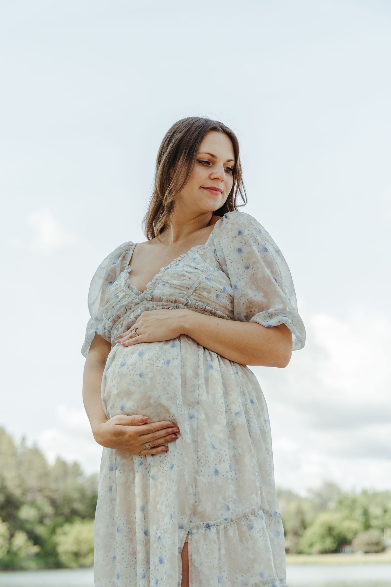 A floral dress maternity photoshoot in a sunny outdoor setting.