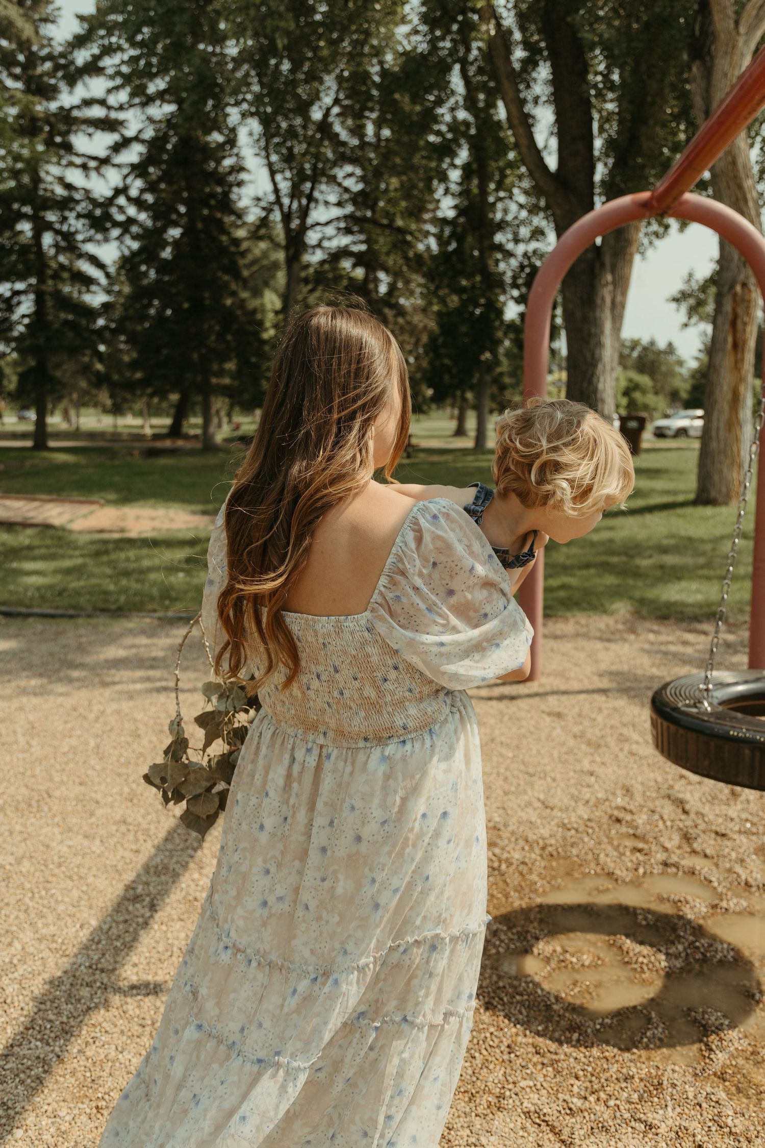 A family plays together at a playground with swings on a sunny afternoon.