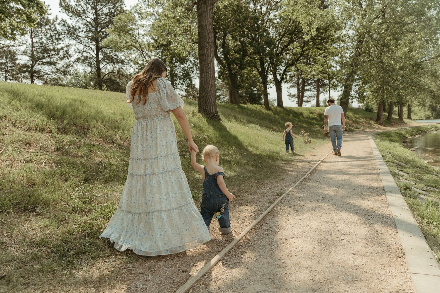 A family strolls down a tree-lined path near a peaceful lake.