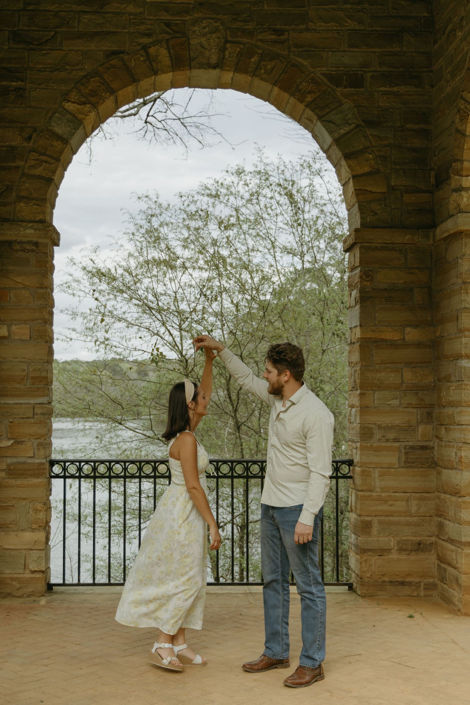 Couple dancing and twirling under a stone archway overlooking scenic views.