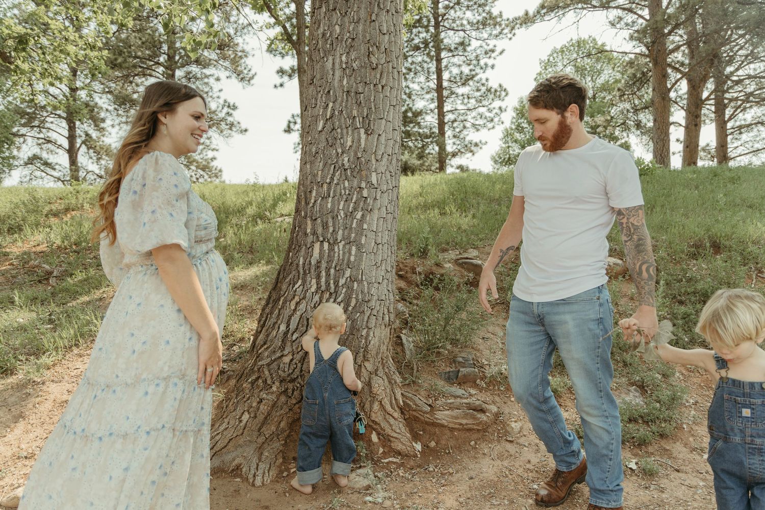 A family explores around a large tree trunk in a natural outdoor setting.