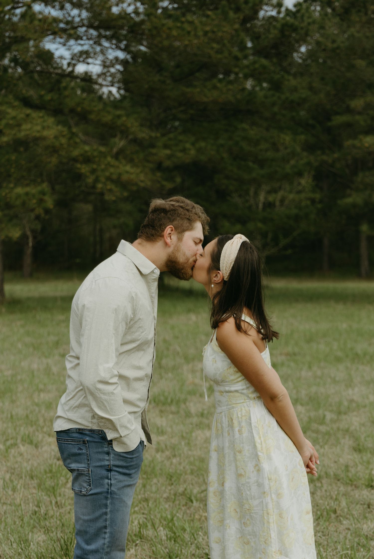 A couple in casual attire shares a sweet moment in a meadow.