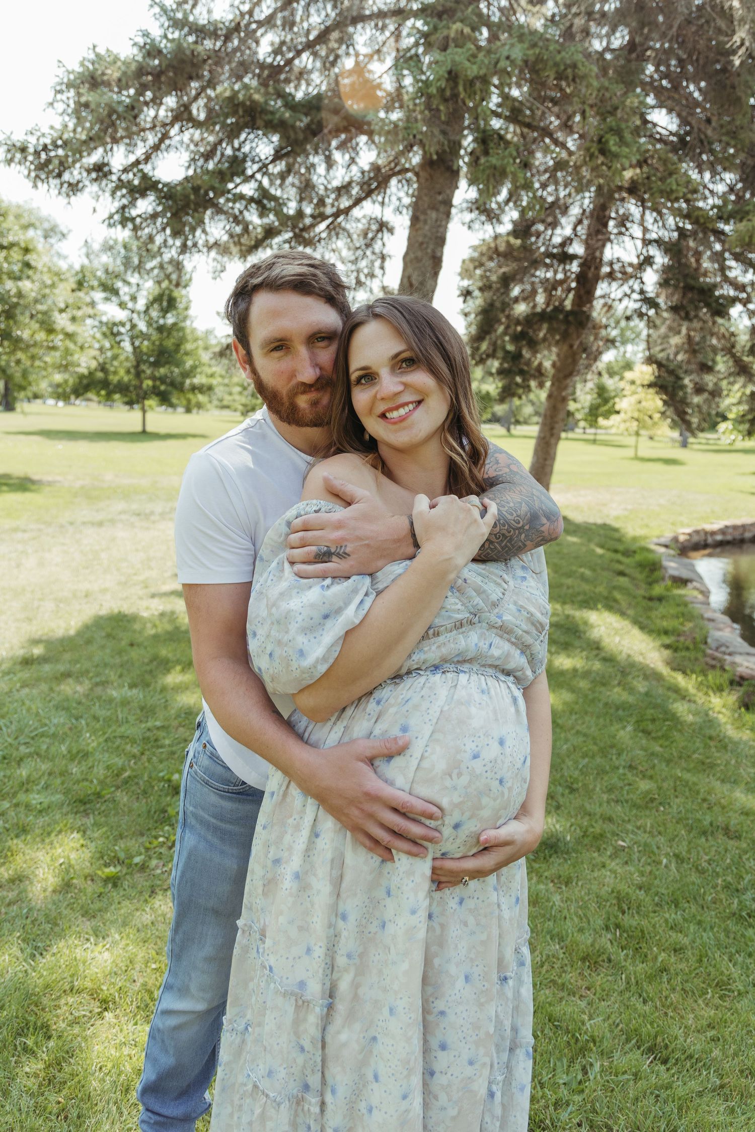 Maternity photos showing loving embrace in a peaceful park setting.
