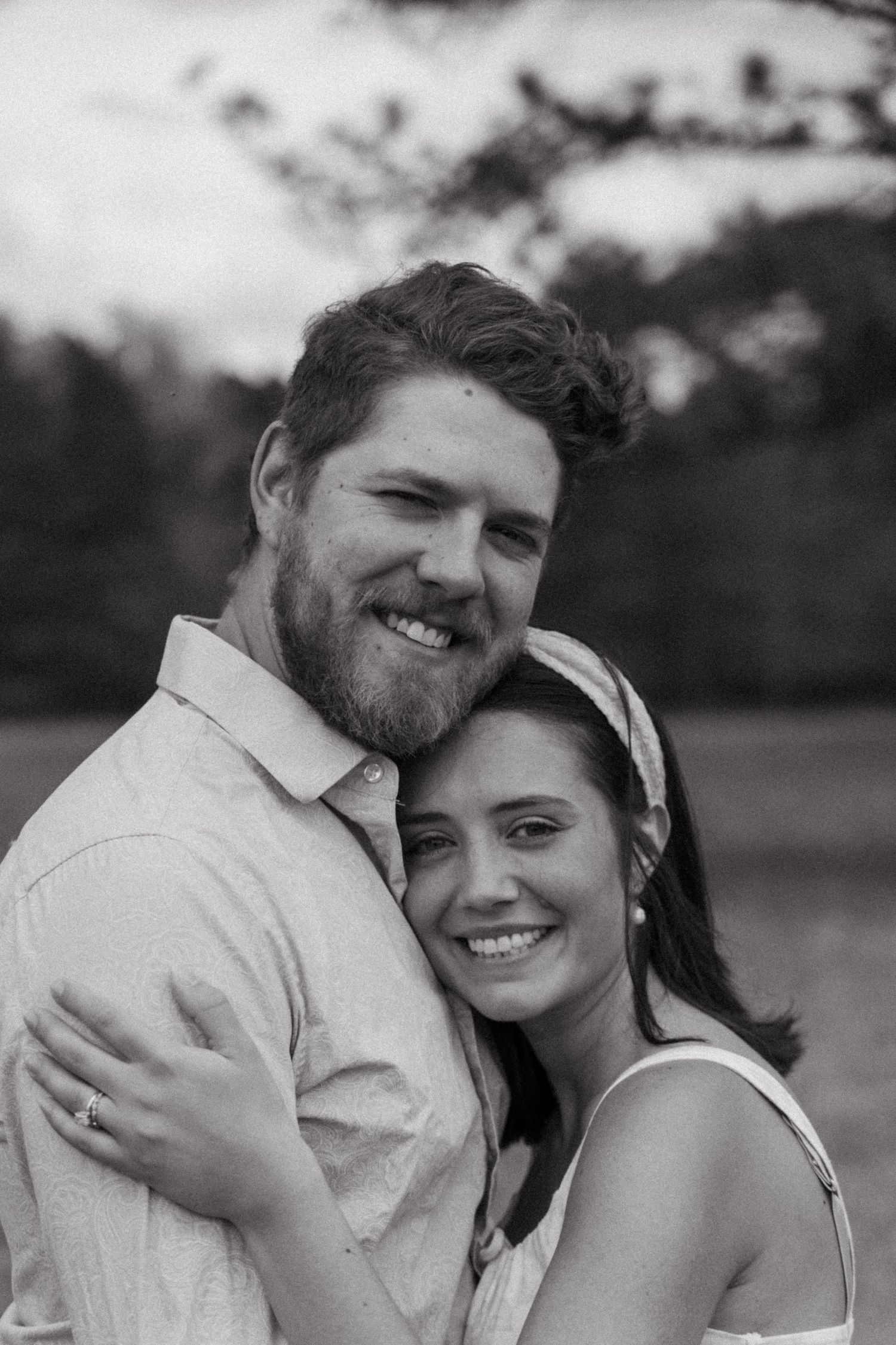 A loving couple embraces outdoors while sharing joyful smiles in a black and white photo series.