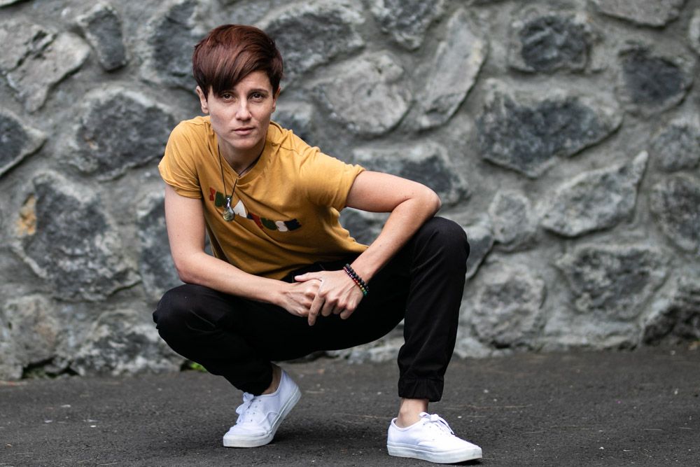 Person in yellow t-shirt crouching against stone wall wearing white sneakers.