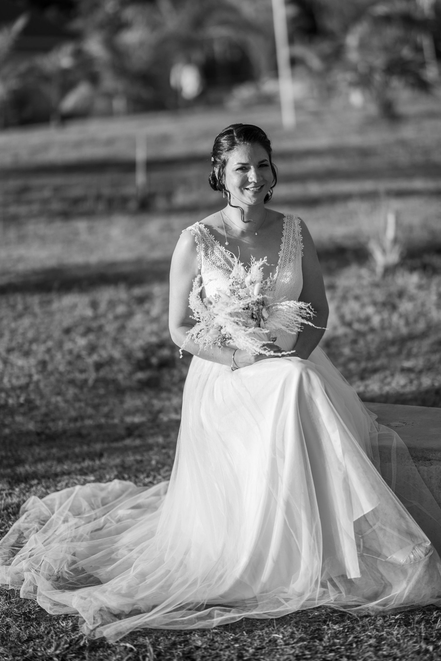 Beautiful black and white portrait of bride in flowing gown holding dried flower bouquet outdoors.