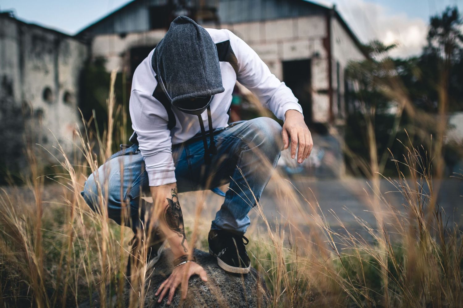 Feet in sneakers and jeans walking along gravel and grass near abandoned buildings.