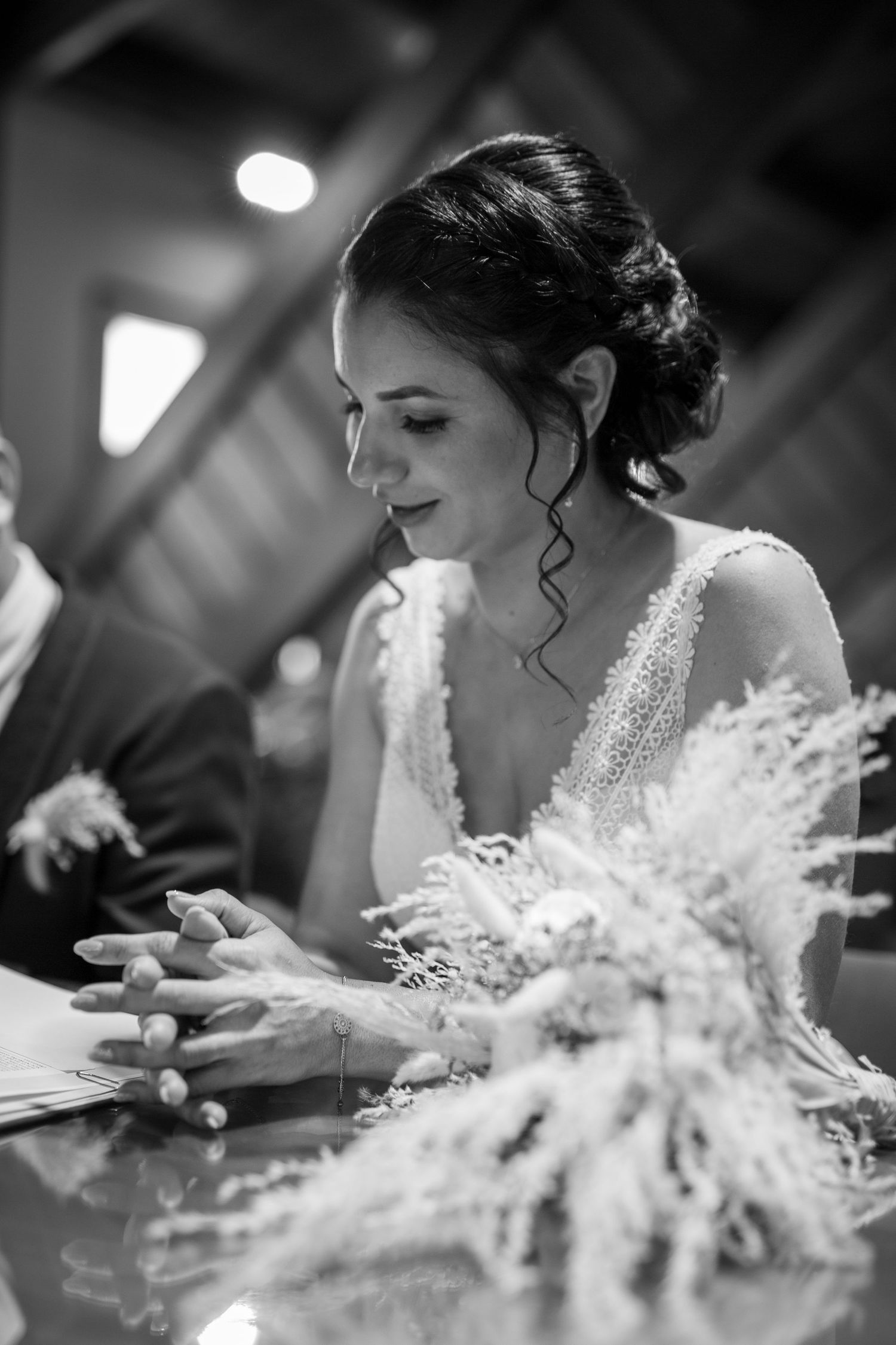 Black and white photo of a bride with an elegant updo signing documents with dried flowers on the table.