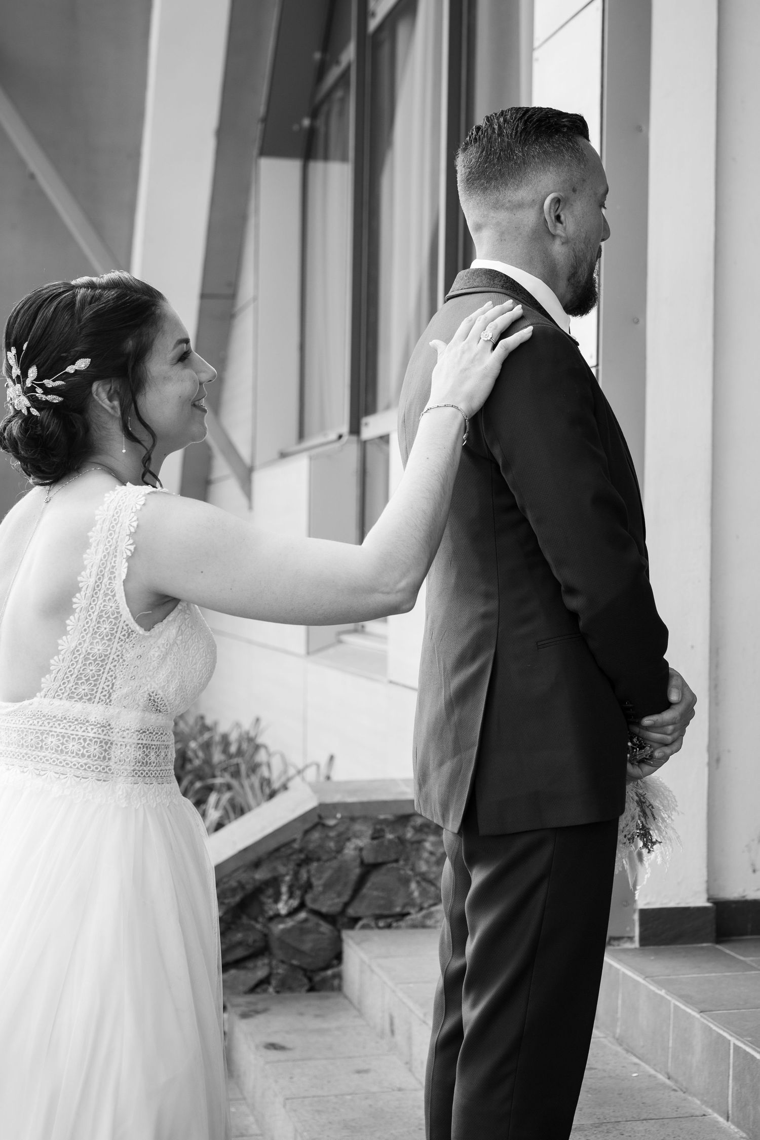 A first look moment at a wedding where a bride in a flowing white dress touches the groom's shoulder from behind.