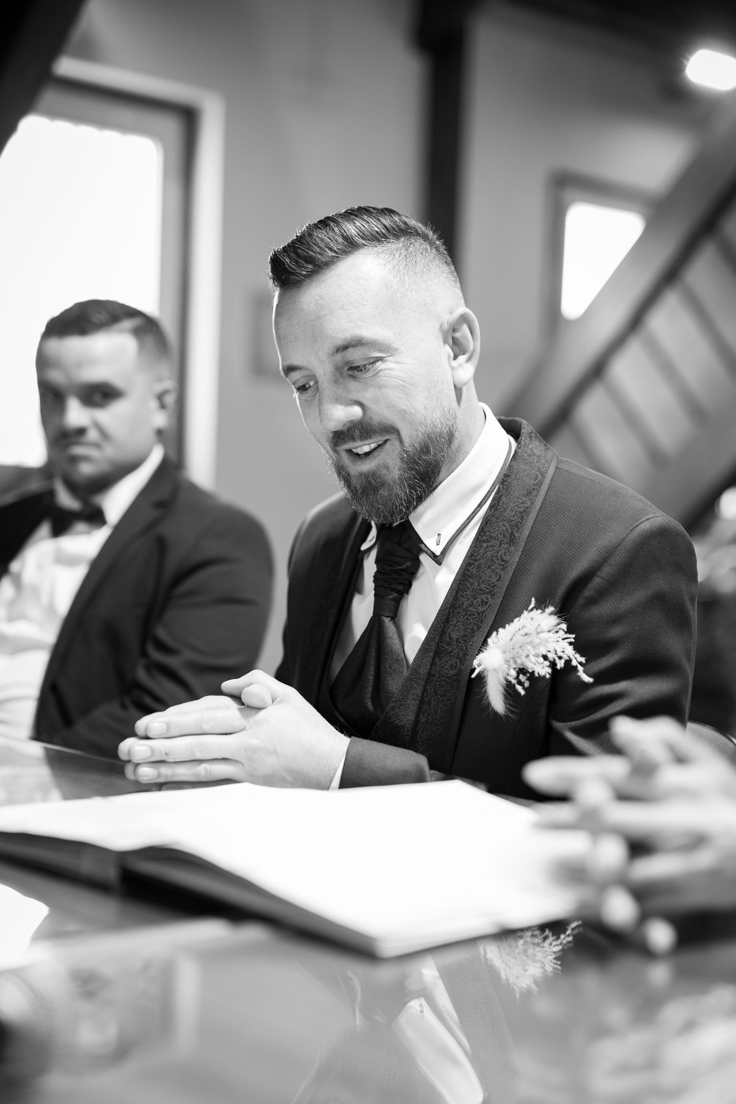 Black and white photo of a smiling groom signing wedding documents at a table.