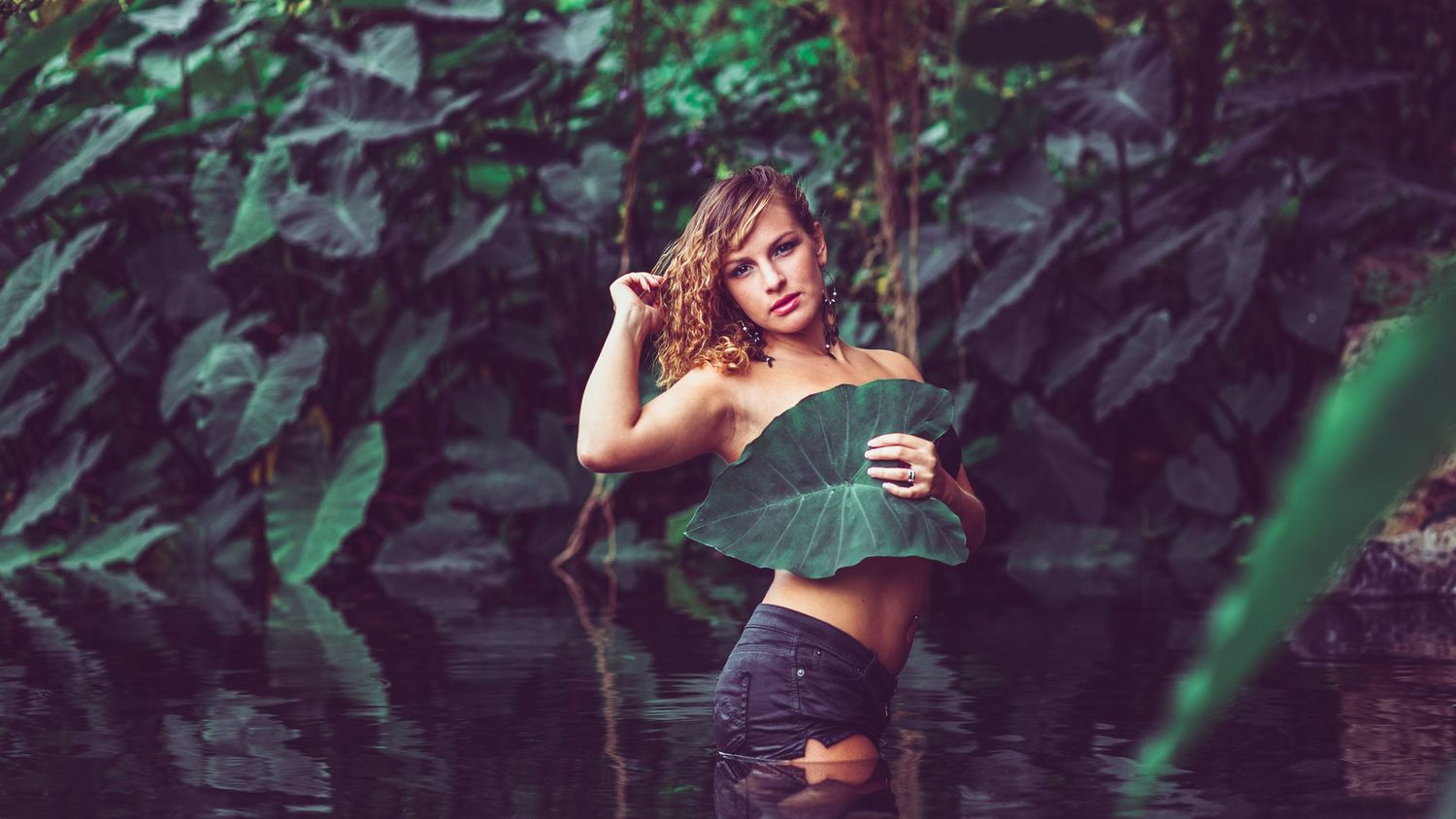 Artistic photo of a model in crop top posing against lush green foliage outdoors.