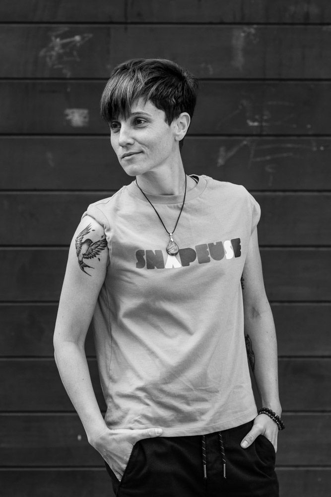 Black and white portrait of person in casual t-shirt with tattoo against wooden wall.