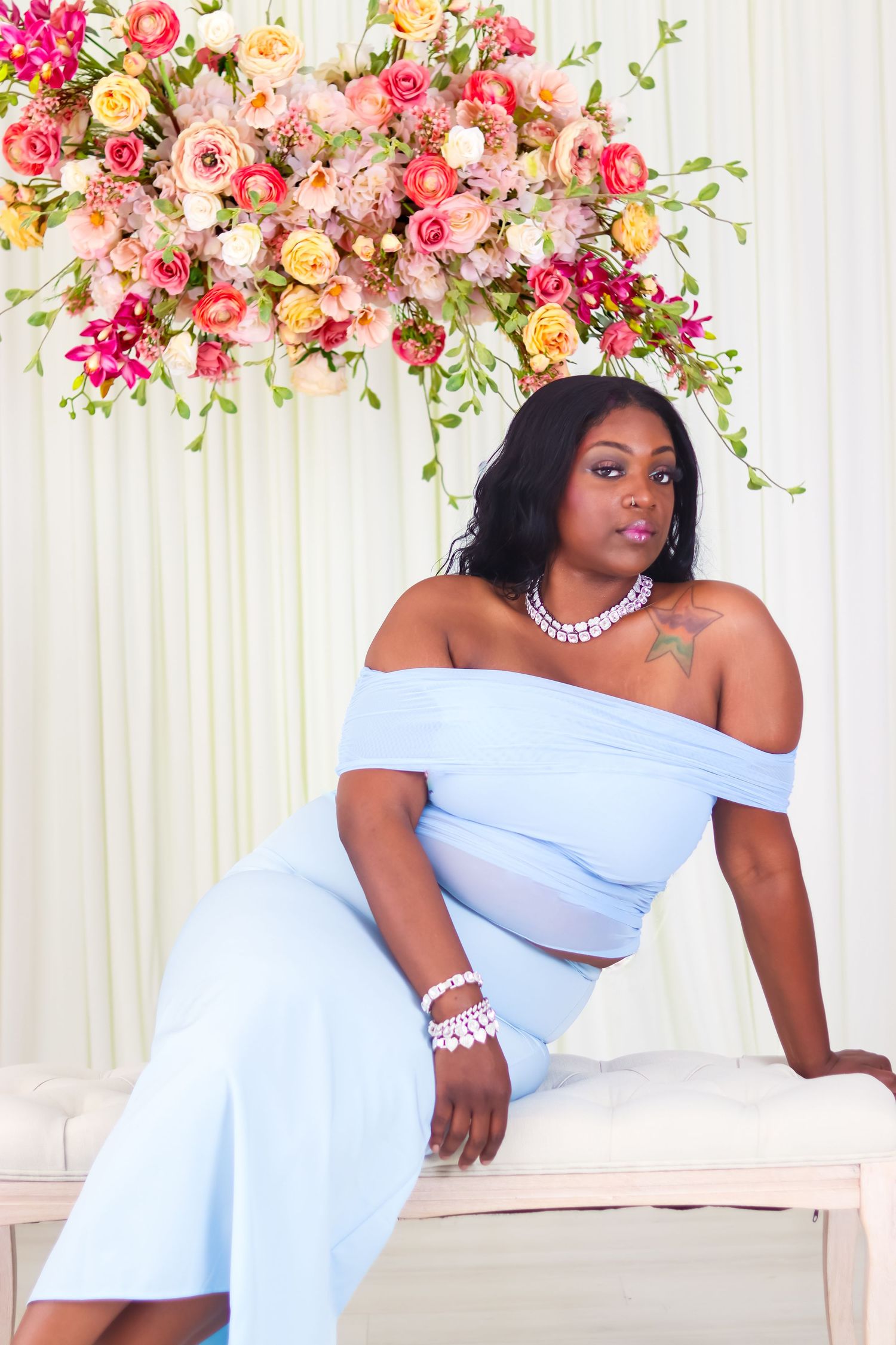 Elegant poses in light blue formal dress against floral backdrop.